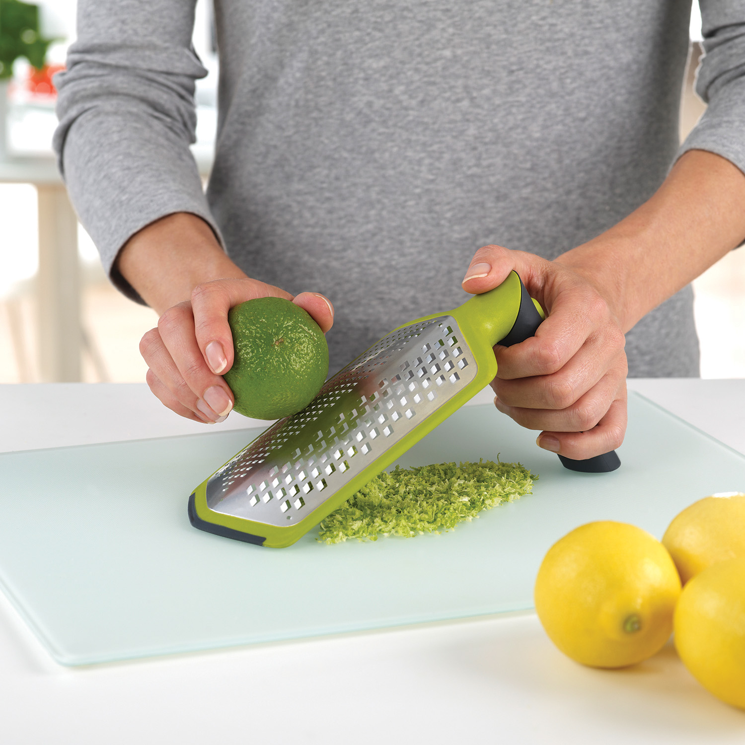 Bir kişi kesme tahtası üzerinde bir rende ile misket limonu rendeliyor.