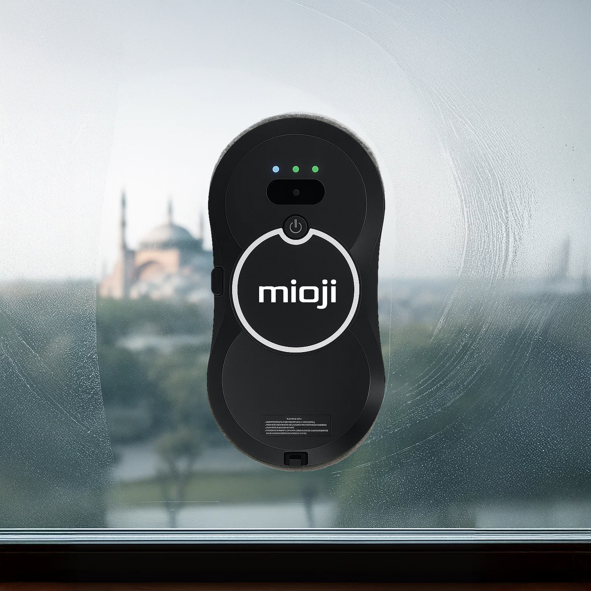 Mioji' logolu siyah pencere temizleme robotu, şehir manzaralı bir pencereyi temizliyor.