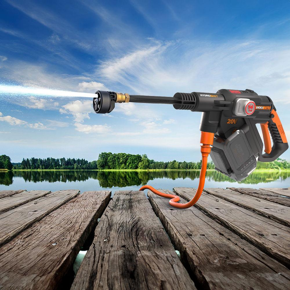 Un'idropulitrice spruzza acqua su un molo di legno con lago e alberi sullo sfondo.
