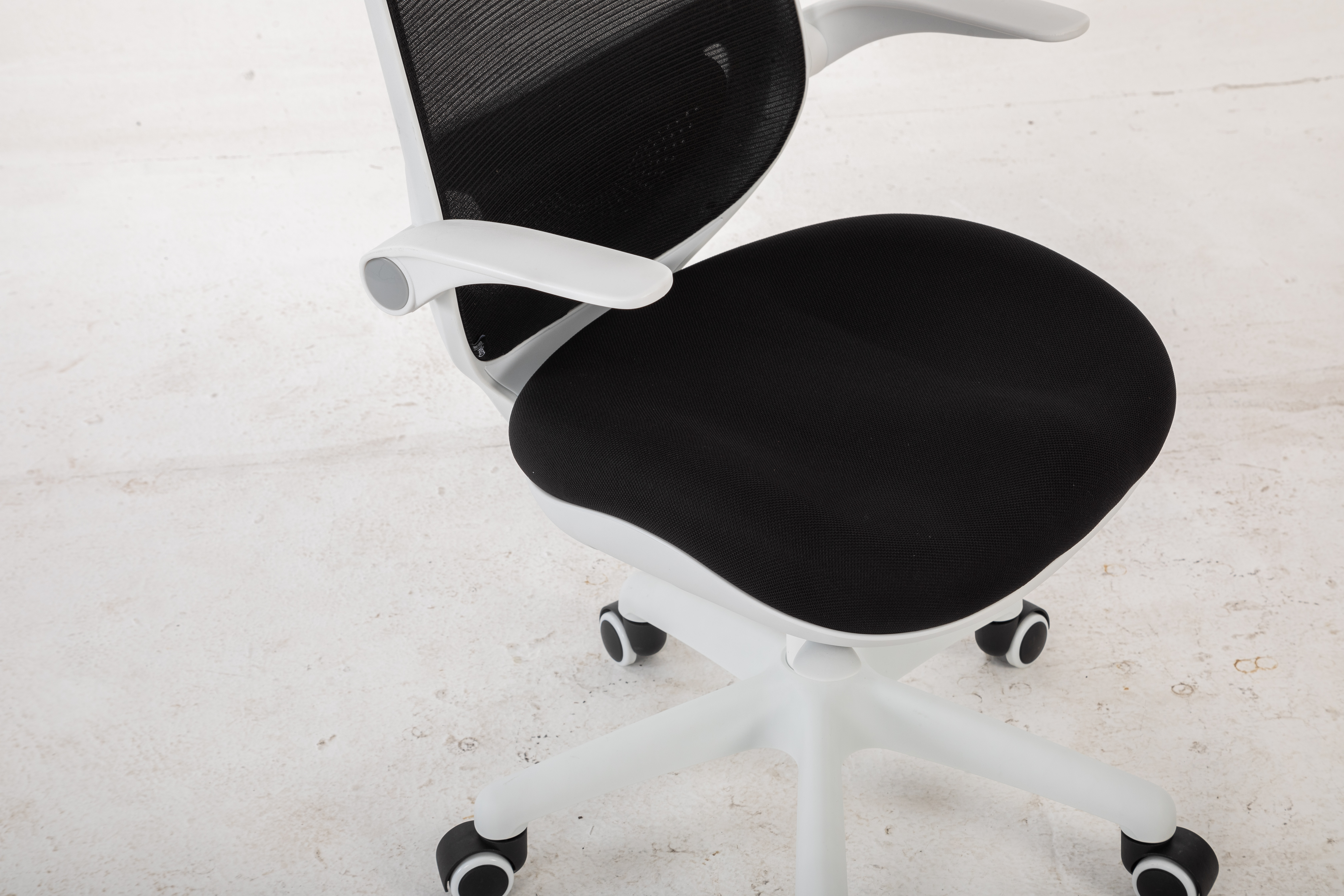 Białe krzesło biurowe z czarnym oparciem i siedziskiem z siatki na kółkach.