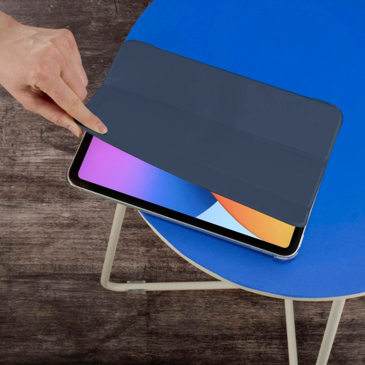 Dłoń zamyka granatową okładkę tabletu na niebieskim stole.