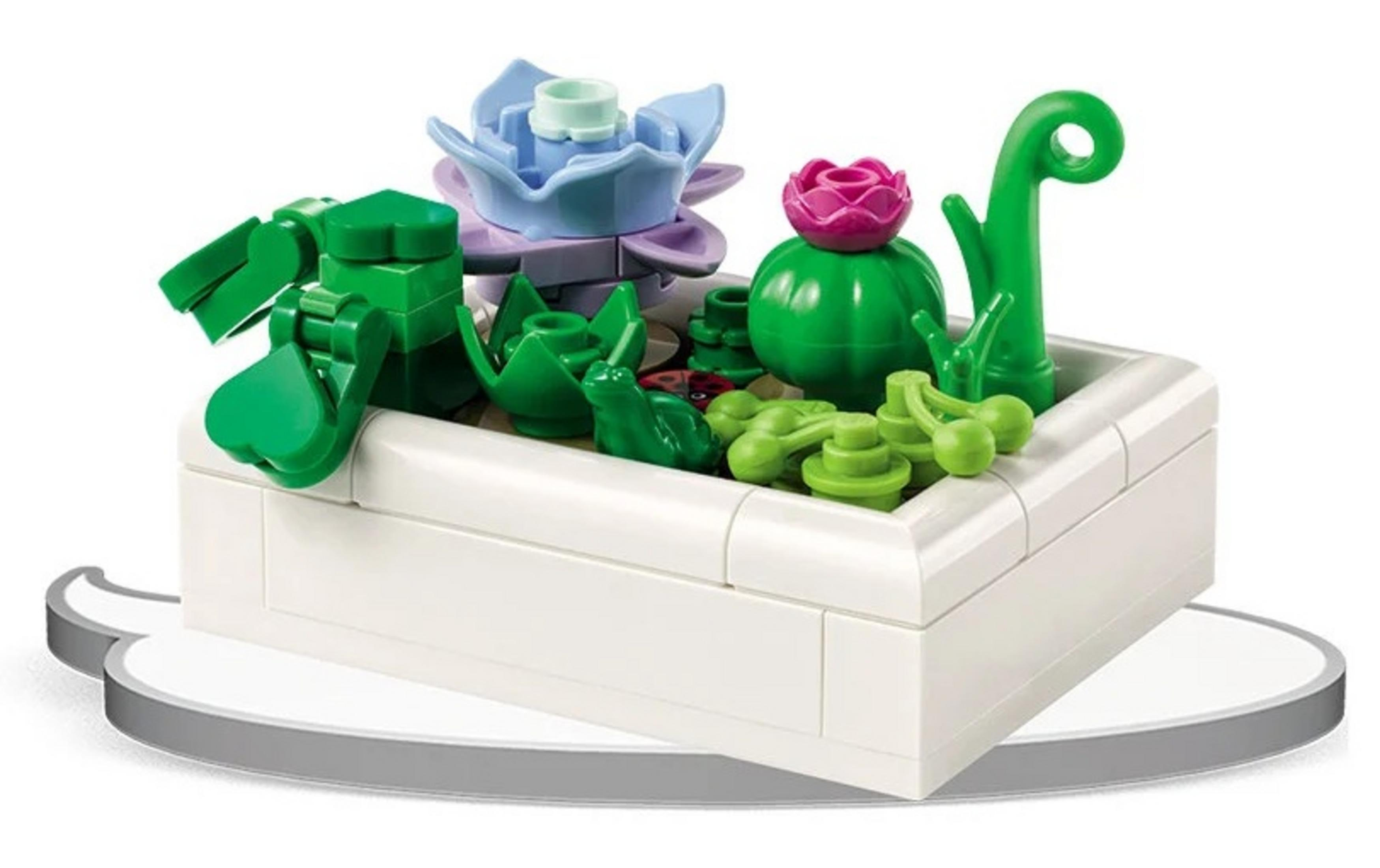 Biały pojemnik z kolorowymi roślinami Lego i żabą.