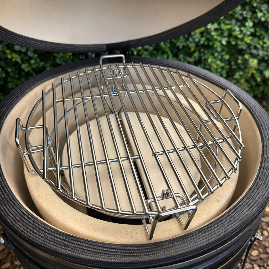 A round metal grill grate sits on a ceramic base with two stone plates.