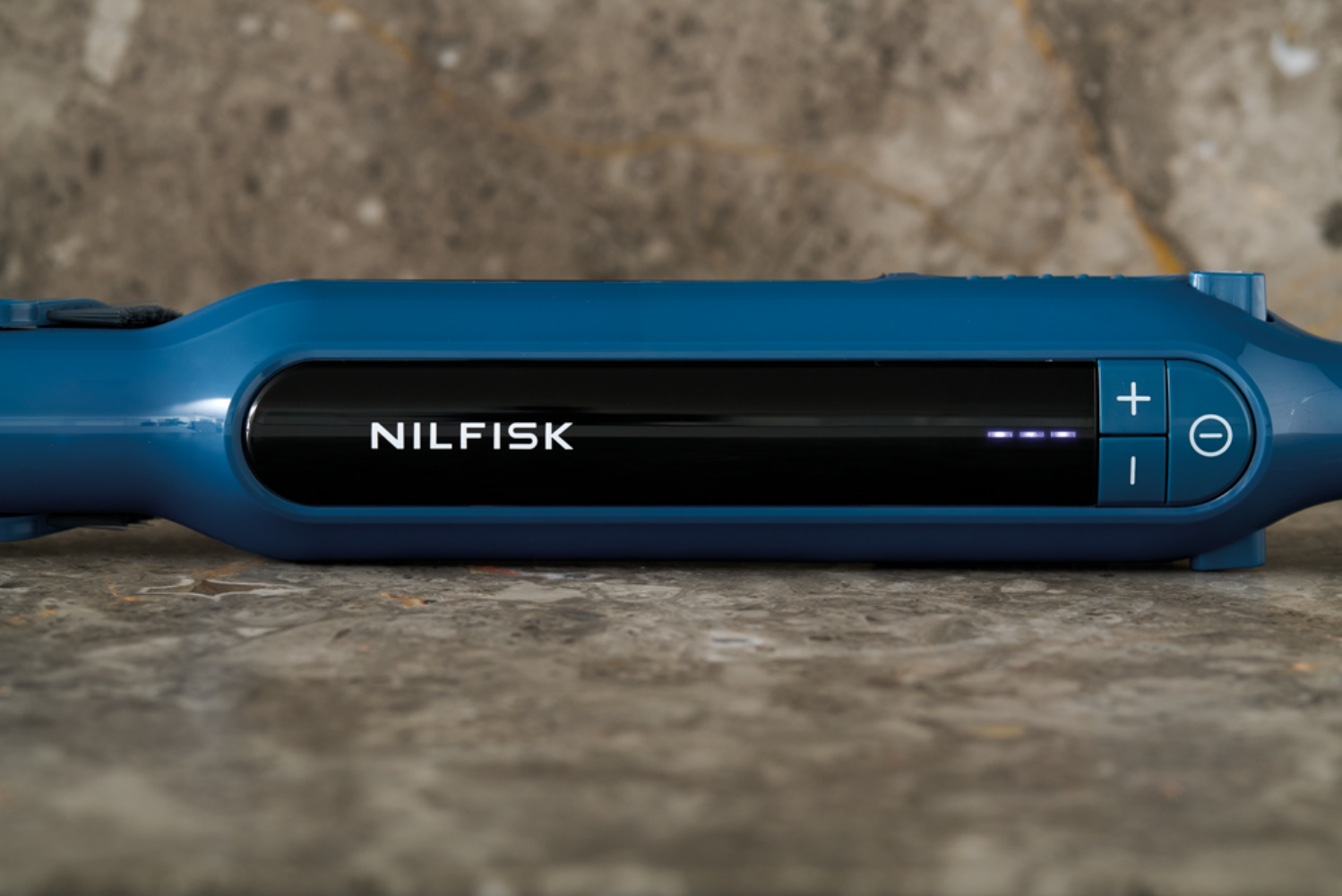 Limpiador NİLFİSK azul con pantalla negra y controles sobre superficie de piedra.