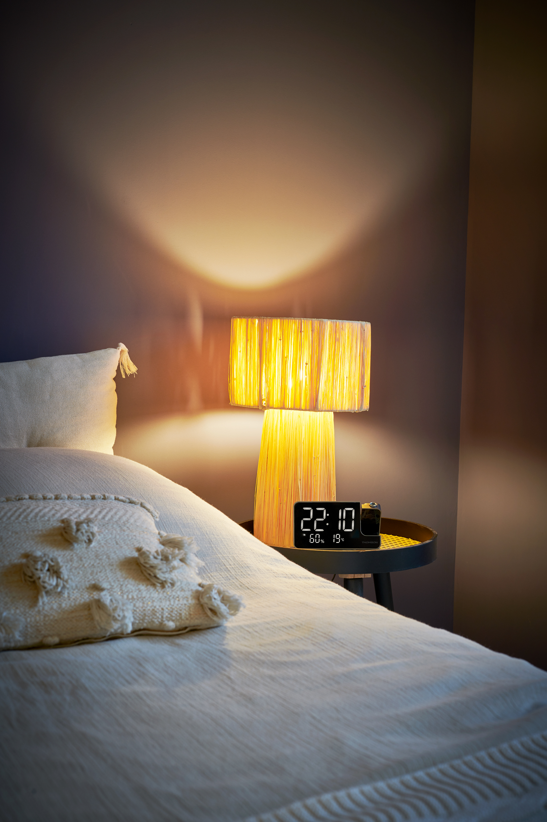 Ein Nachttisch mit Lampe und Uhr neben einem Bett mit Kissen.