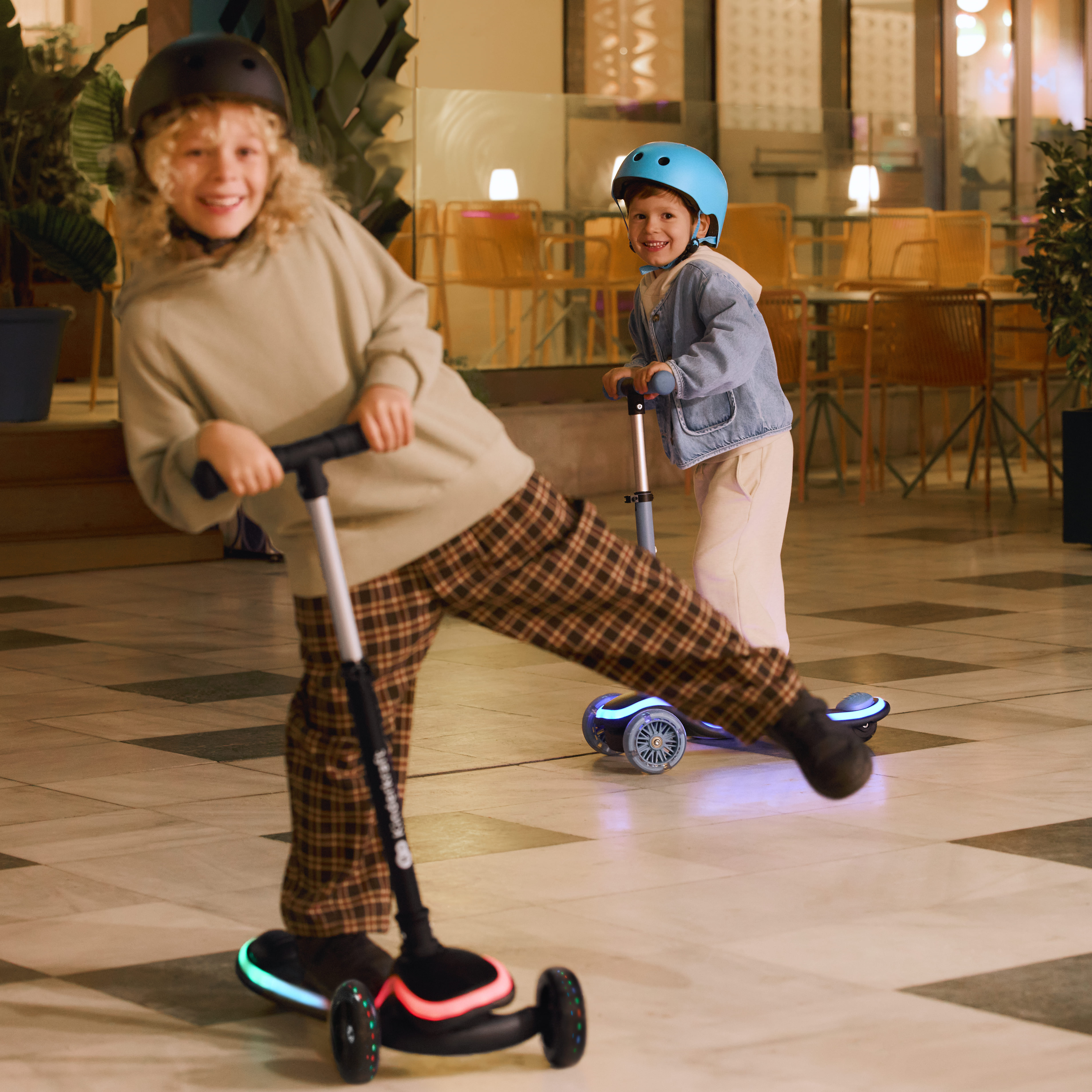 Zwei Kinder fahren Roller mit leuchtenden Rädern in einem Einkaufszentrum.