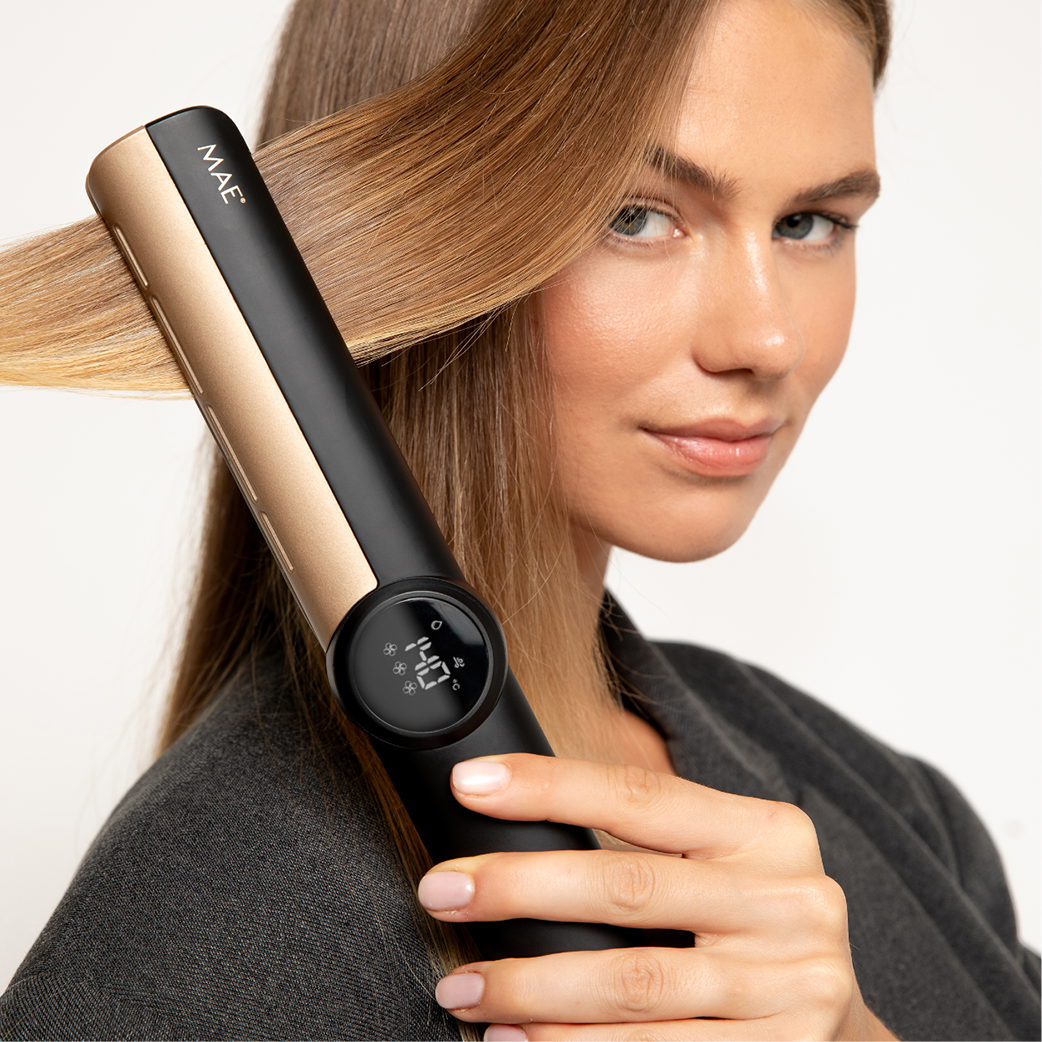 A woman straightens her blonde hair with a black and gold hair straightener.