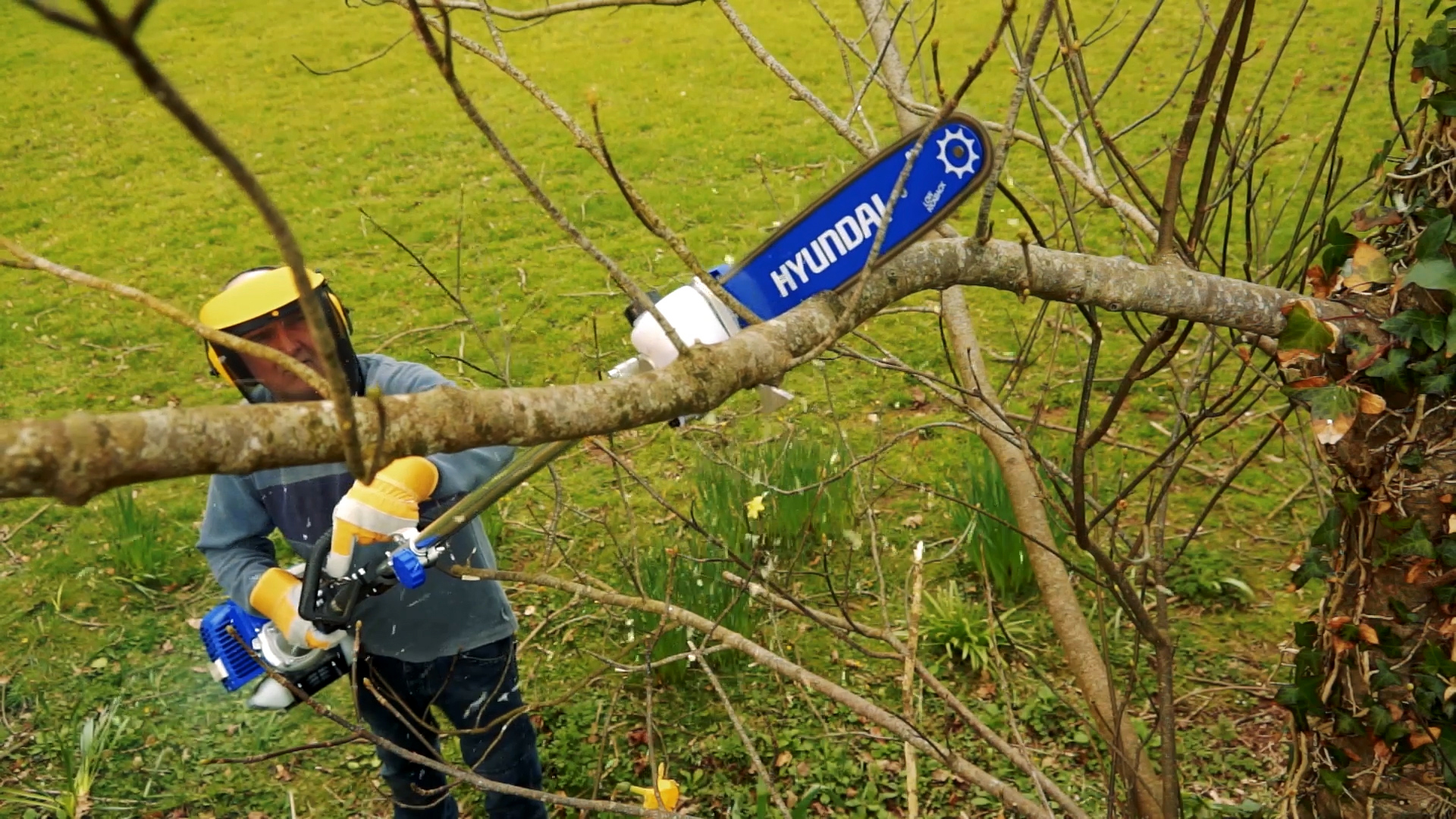 Hombre con motosierra corta rama de árbol en jardín verde.