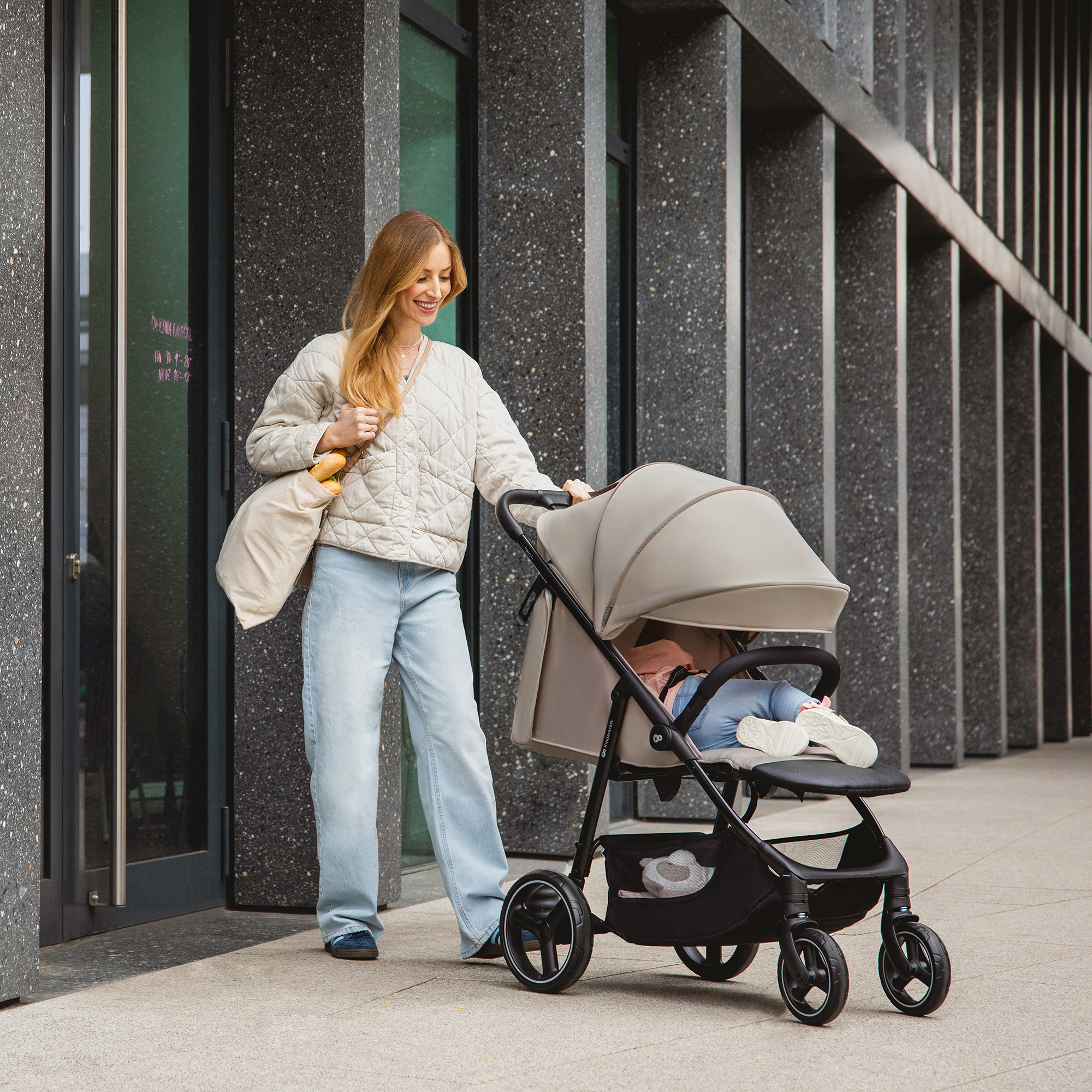 Eine Frau schiebt einen Kinderwagen vor einem modernen Gebäude mit Granitfassade.