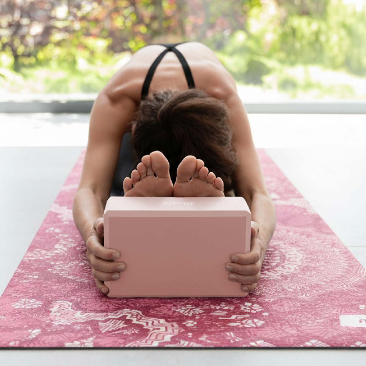 Una persona se estira en una esterilla de yoga rosa, con un bloque rosa bajo los pies.