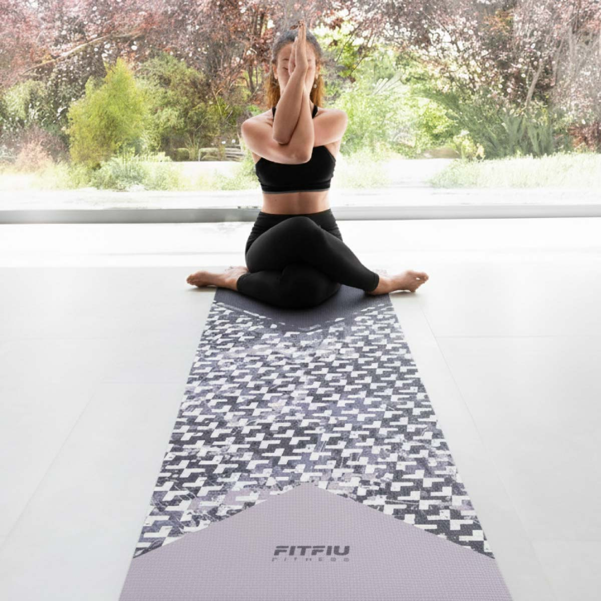 Una mujer de negro practica yoga en una esterilla frente a una ventana con árboles.