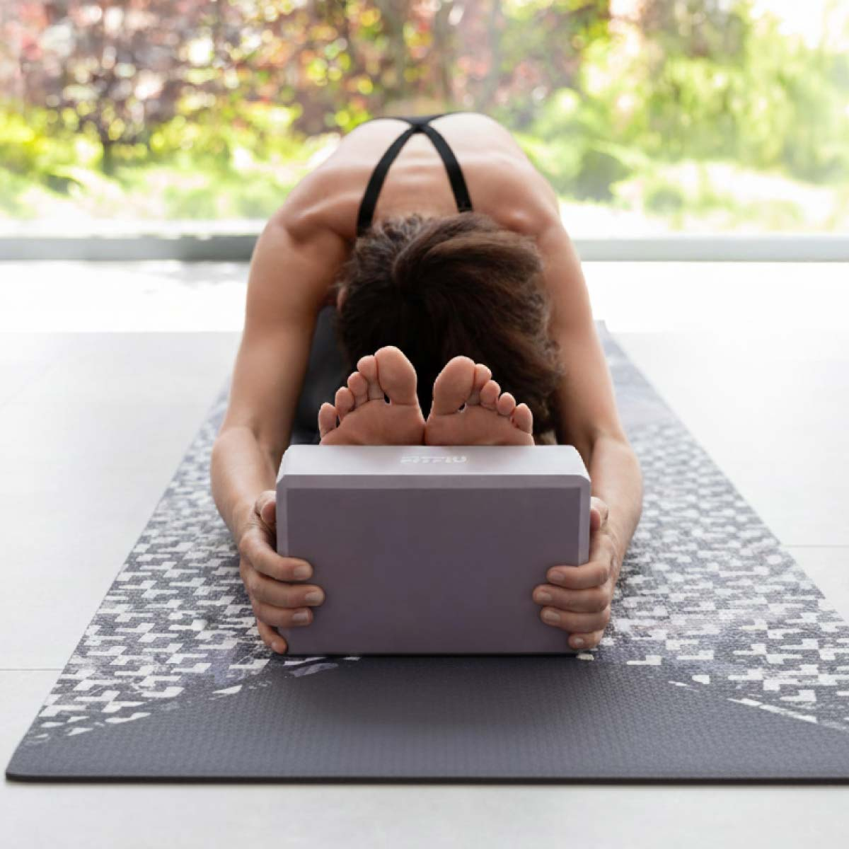 Una persona se estira en una esterilla de yoga, la frente apoyada en un bloque.