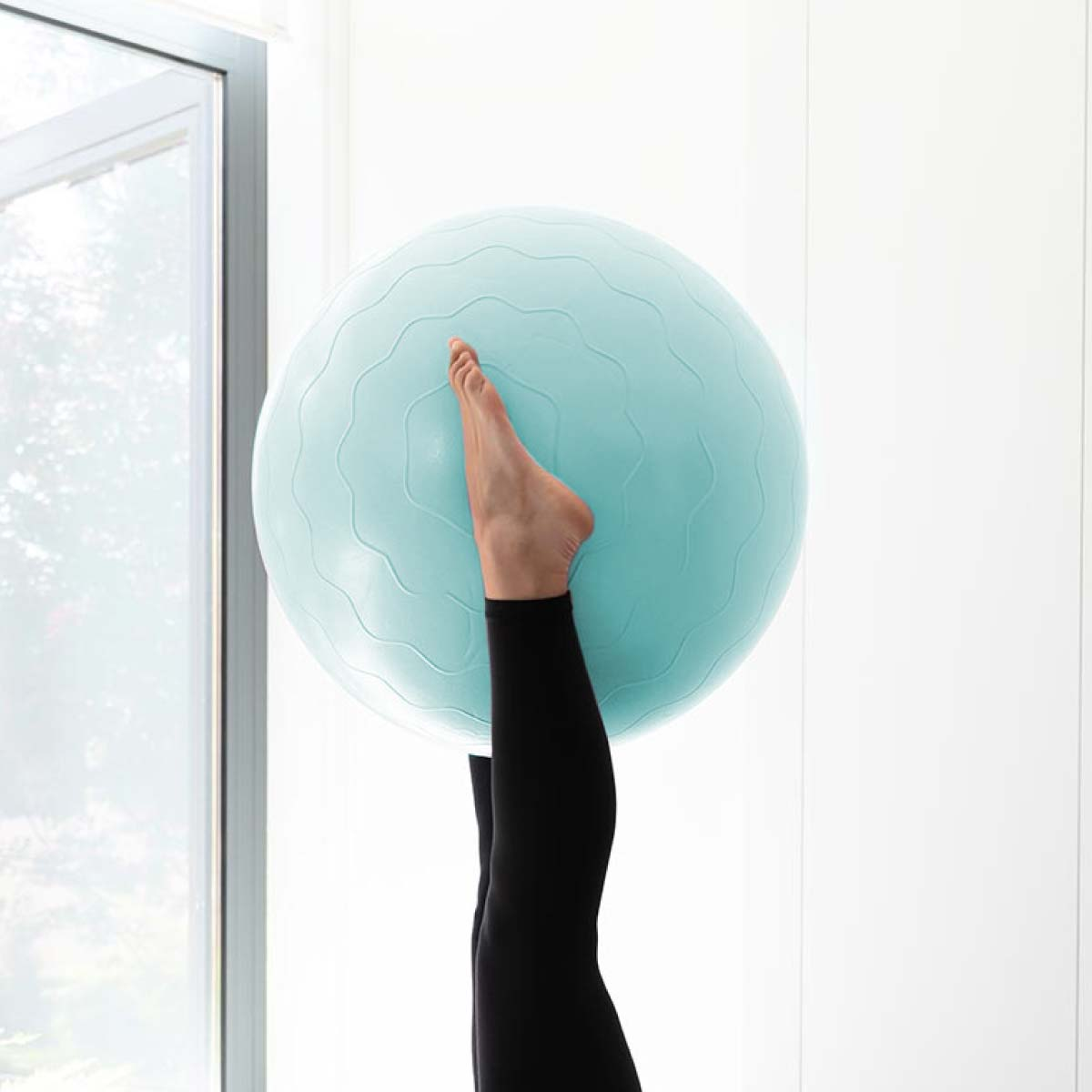 Pie y piernas de una persona equilibrándose sobre una pelota de ejercicio azul claro.