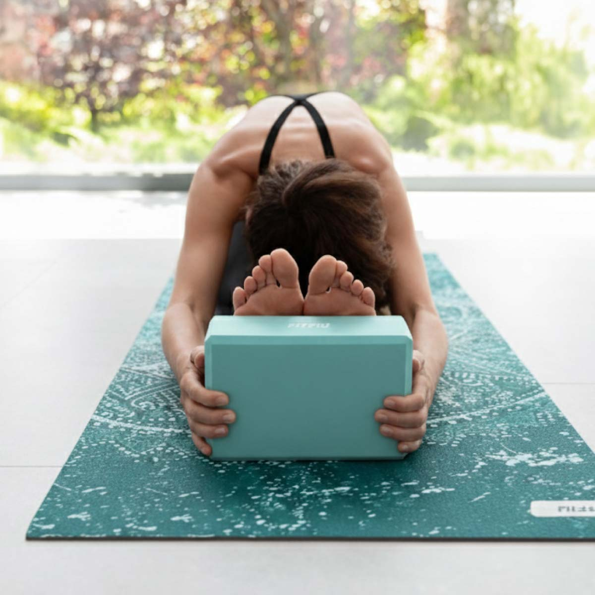 Una mujer en postura de yoga con un bloque azul delante.