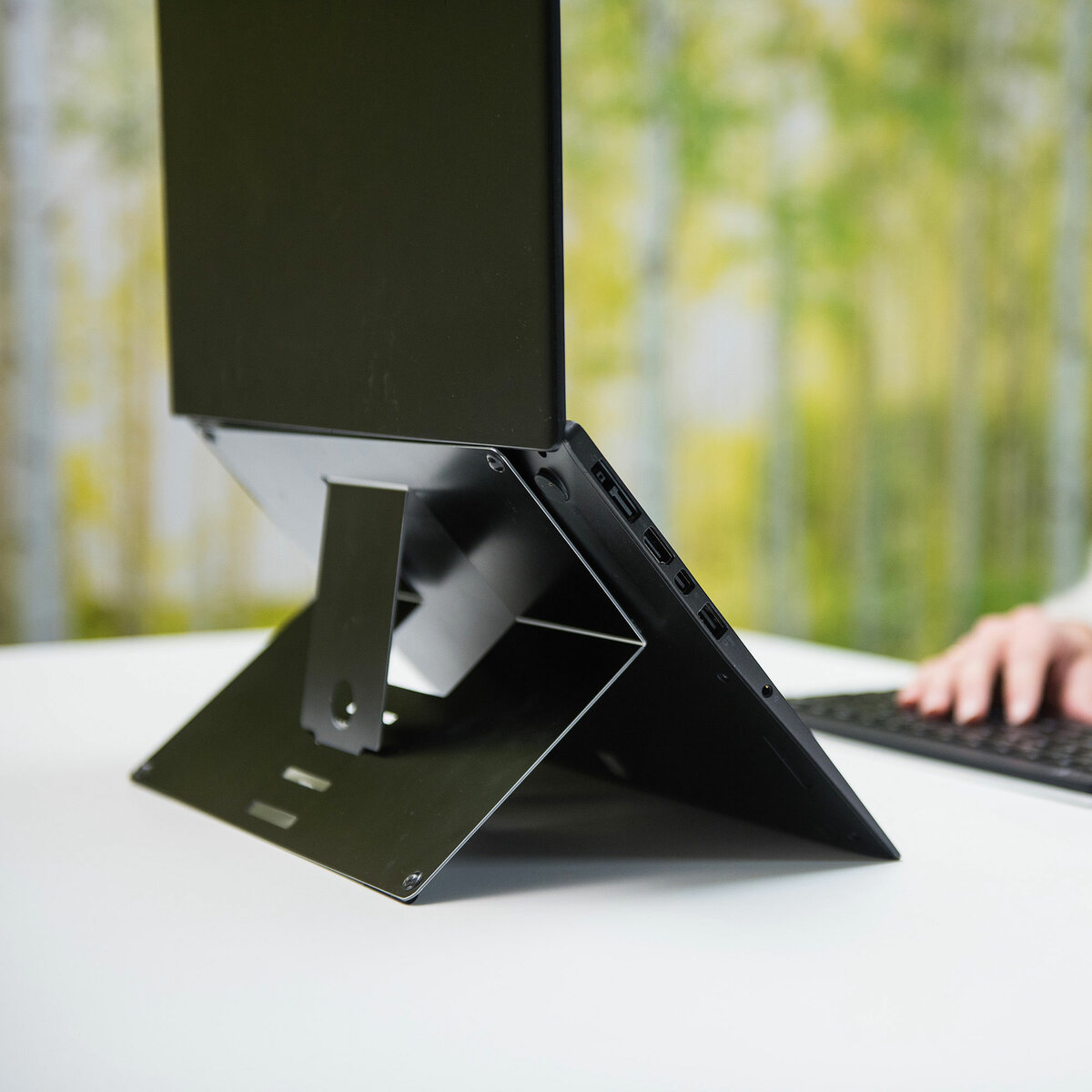 Ein schwarzer Laptop steht auf einem Metallständer mit unscharfem Hintergrund von Bäumen.
