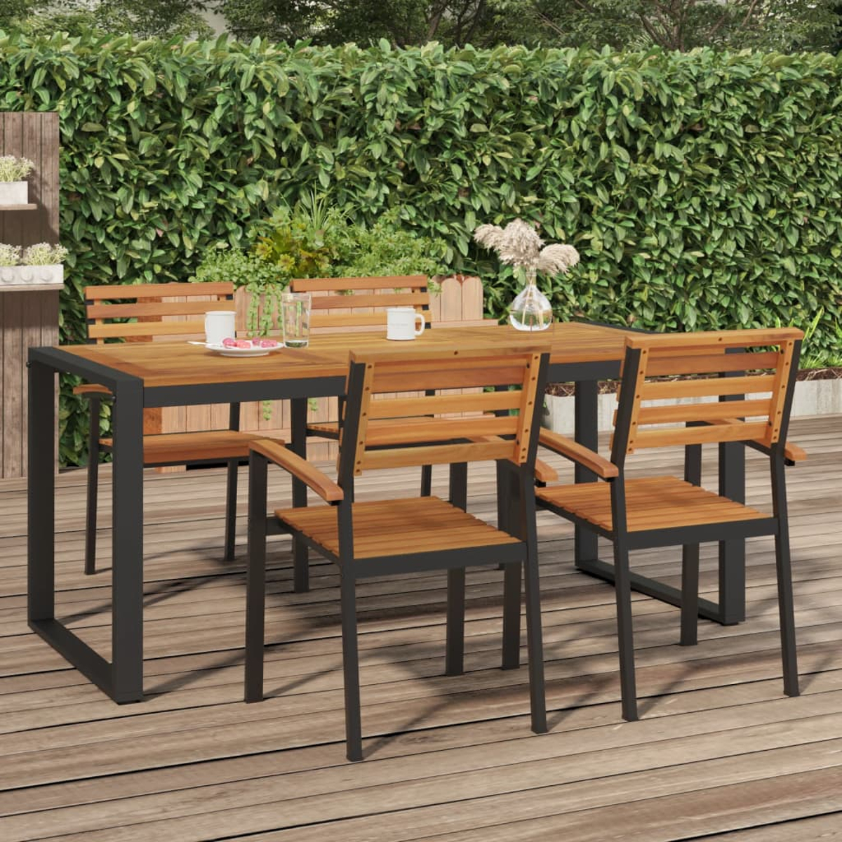 Holztisch und Stühle auf einer Holzterrasse vor einer grünen Hecke.