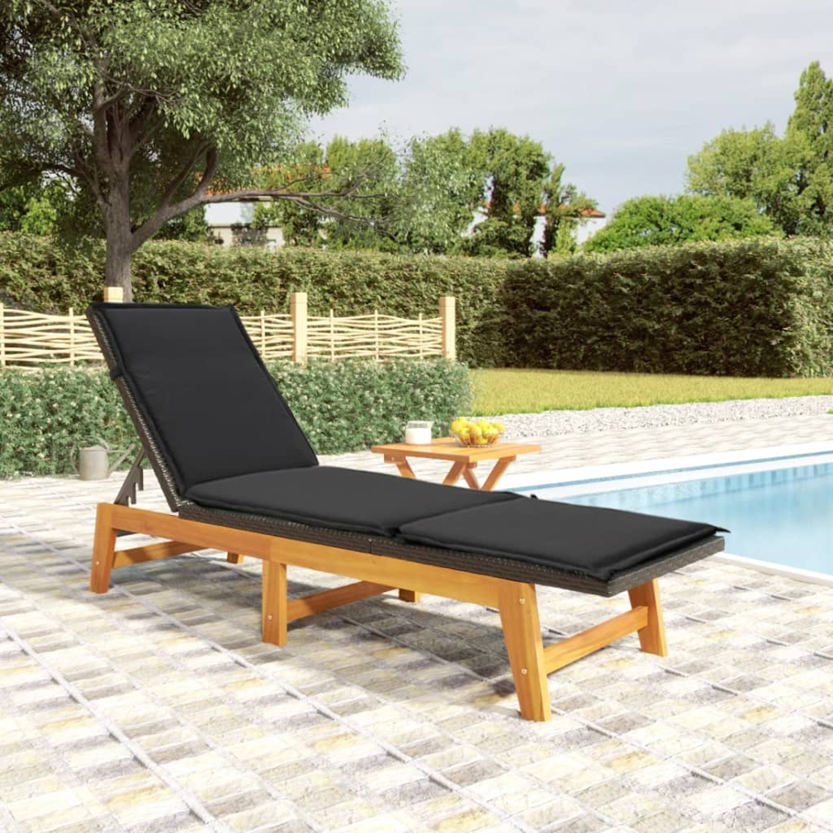 Holzliege mit schwarzem Kissen am Pool mit Obstschale und kleinem Tisch.