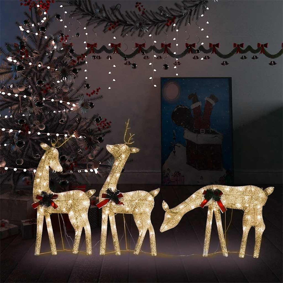 Drei leuchtende Rentier-Dekorationen mit roten Schleifen stehen vor einem Weihnachtsbaum.