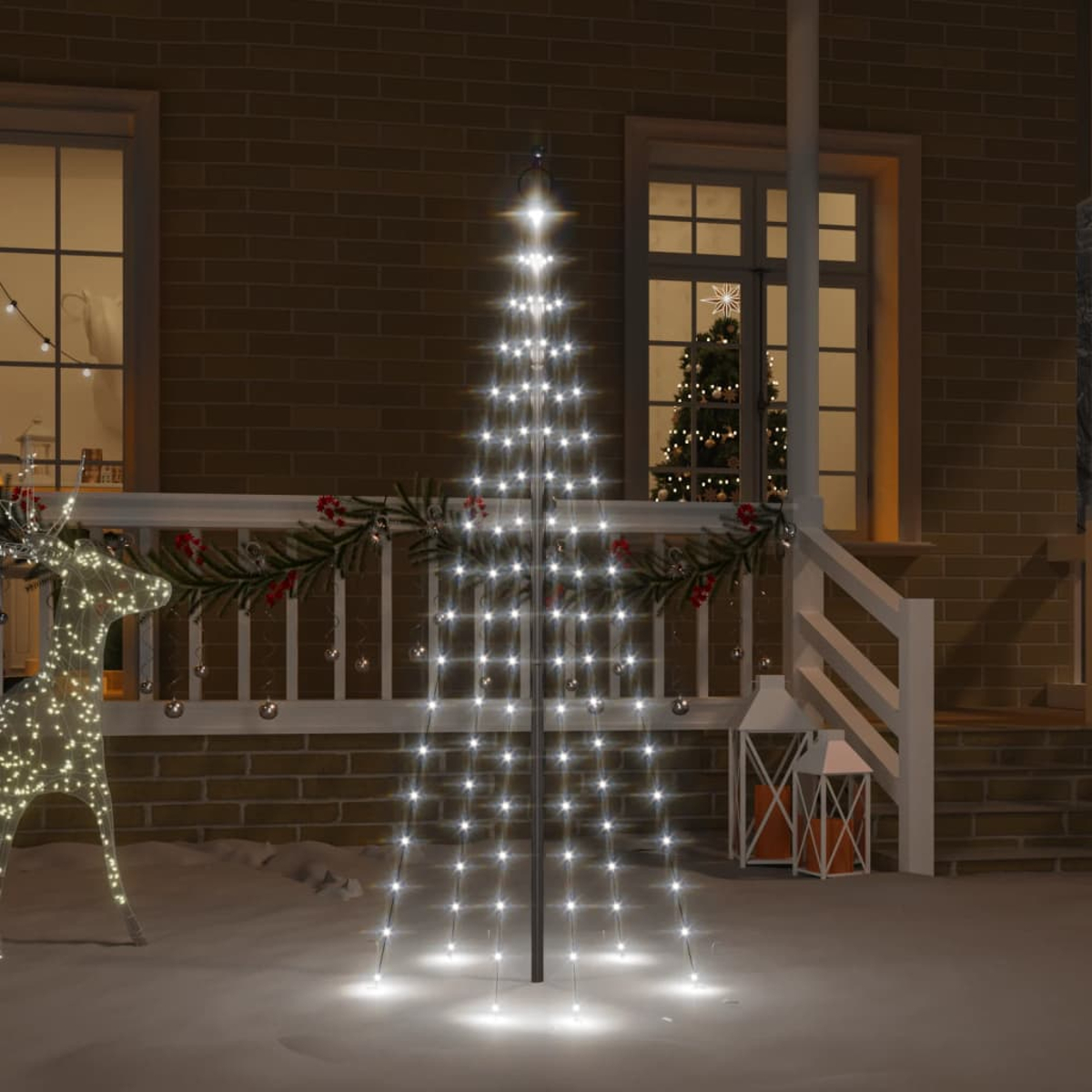 Ein beleuchteter Baum und ein Rentier stehen vor einem Haus, Schnee liegt.