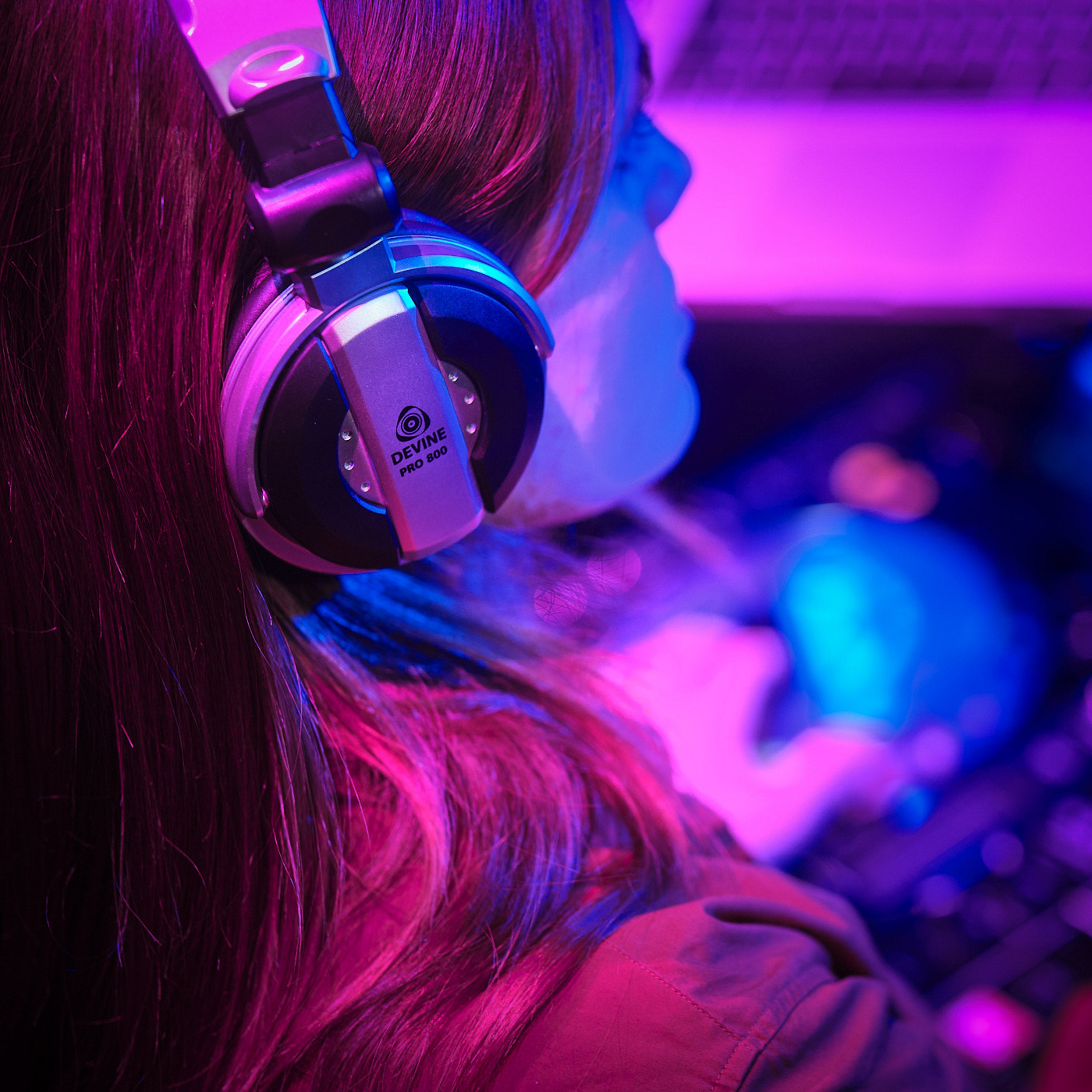 A person wearing headphones, illuminated by pink and blue light.