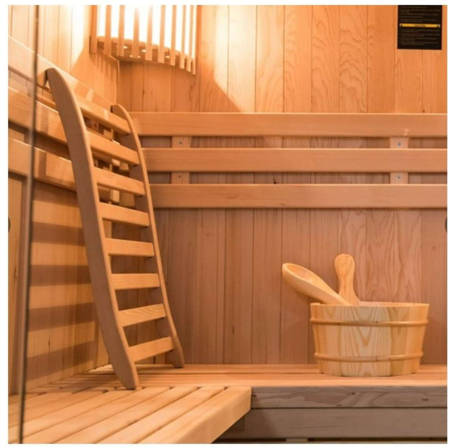 Sauna de madera con dos niveles, escalera y cubo de madera con cucharón.