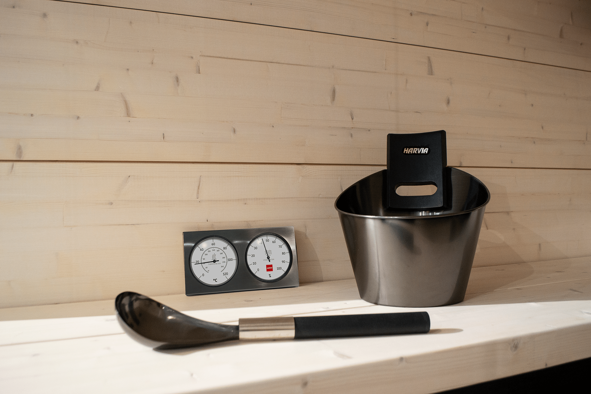 Accesorios de sauna: un cubo metálico con pala Harvia, un termómetro y un higrómetro.