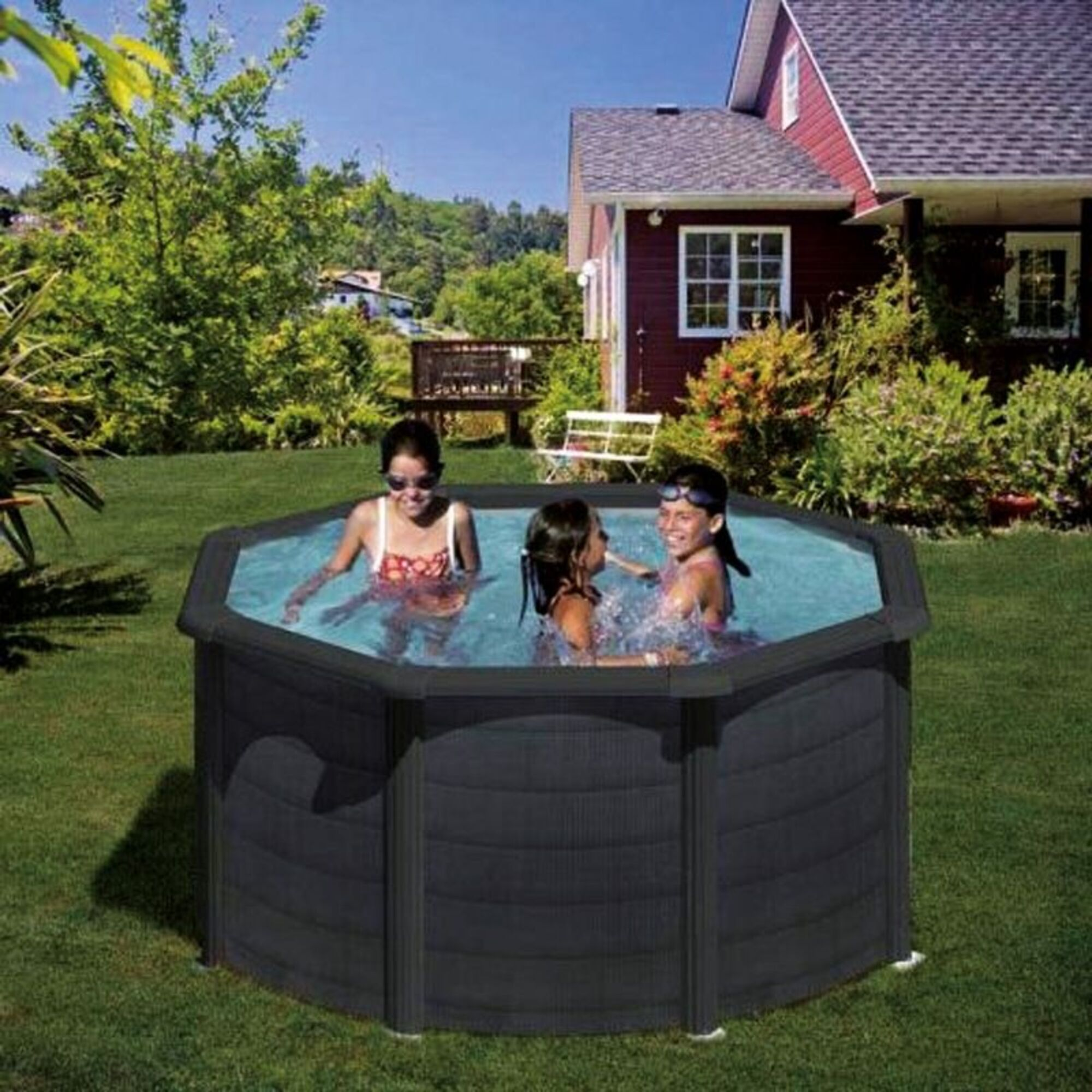 Tres niñas chapotean en una piscina redonda en un jardín. Una casa al fondo.