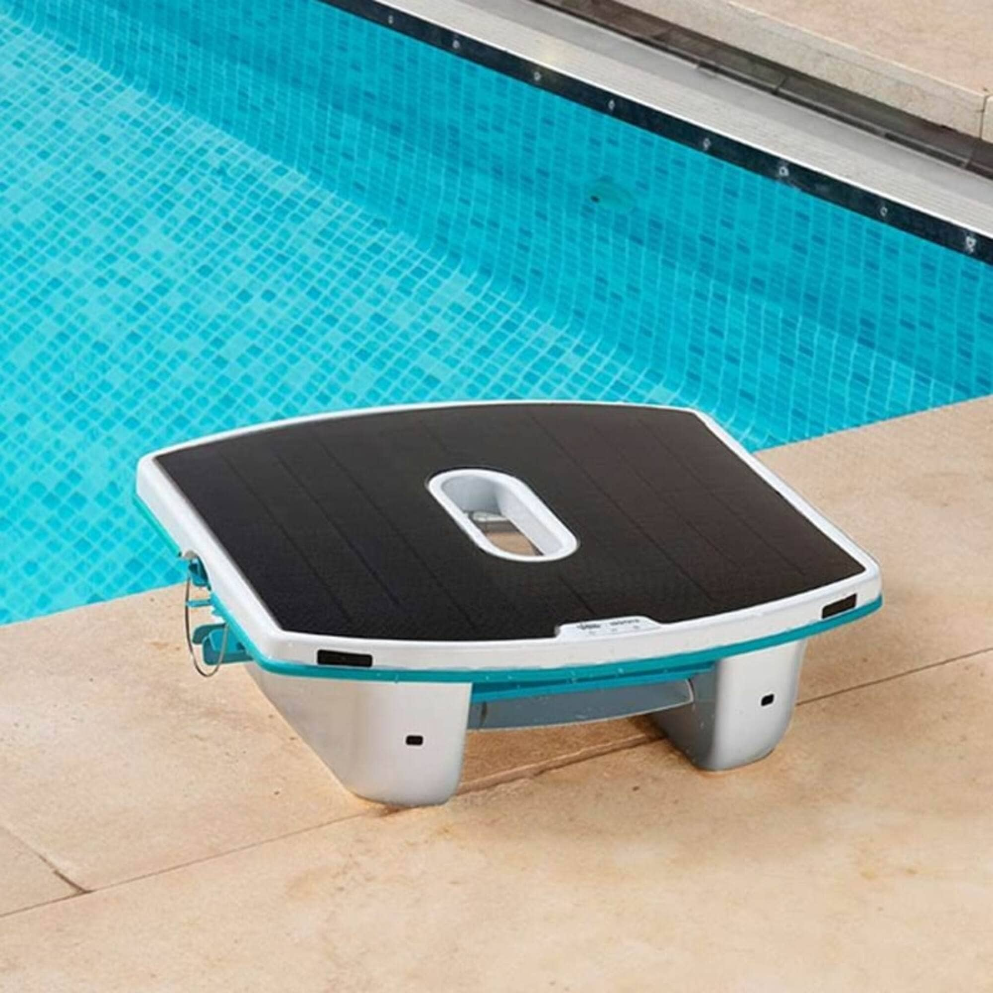 Un robot pulitore per piscine bianco e nero con finiture blu si trova su una piastrella chiara accanto a una piscina piastrellata di blu.