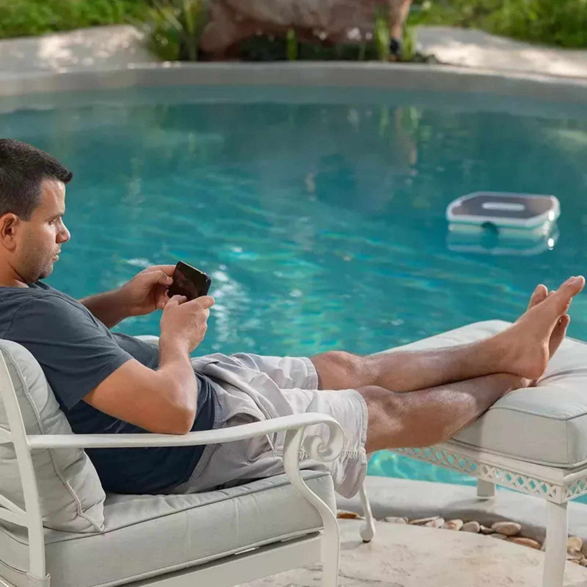 Hombre relajándose en la piscina mientras un robot limpia el agua.