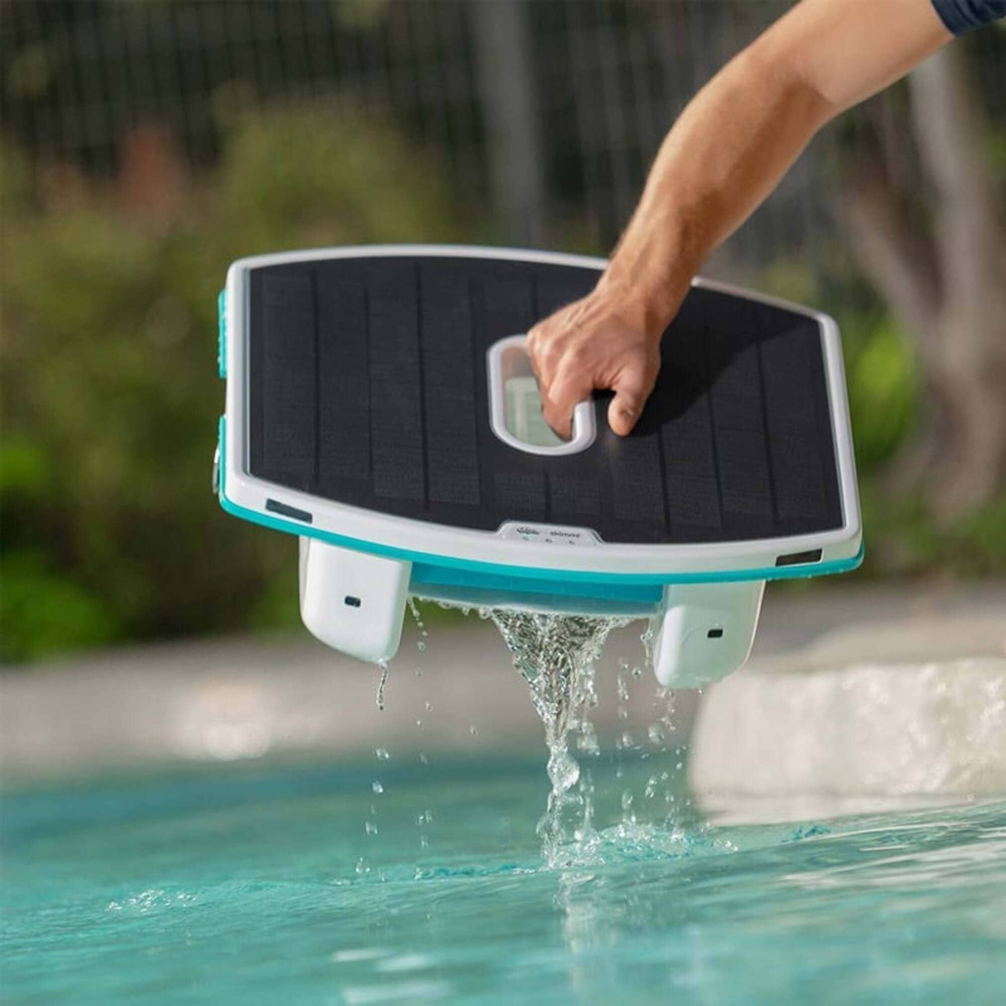 Una mano levanta un robot de piscina del agua, goteando agua.