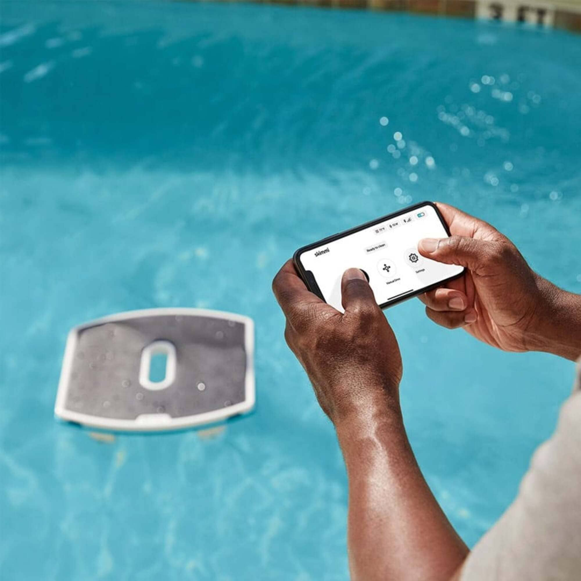 Un uomo aziona un robot da piscina con il suo smartphone in una piscina blu.