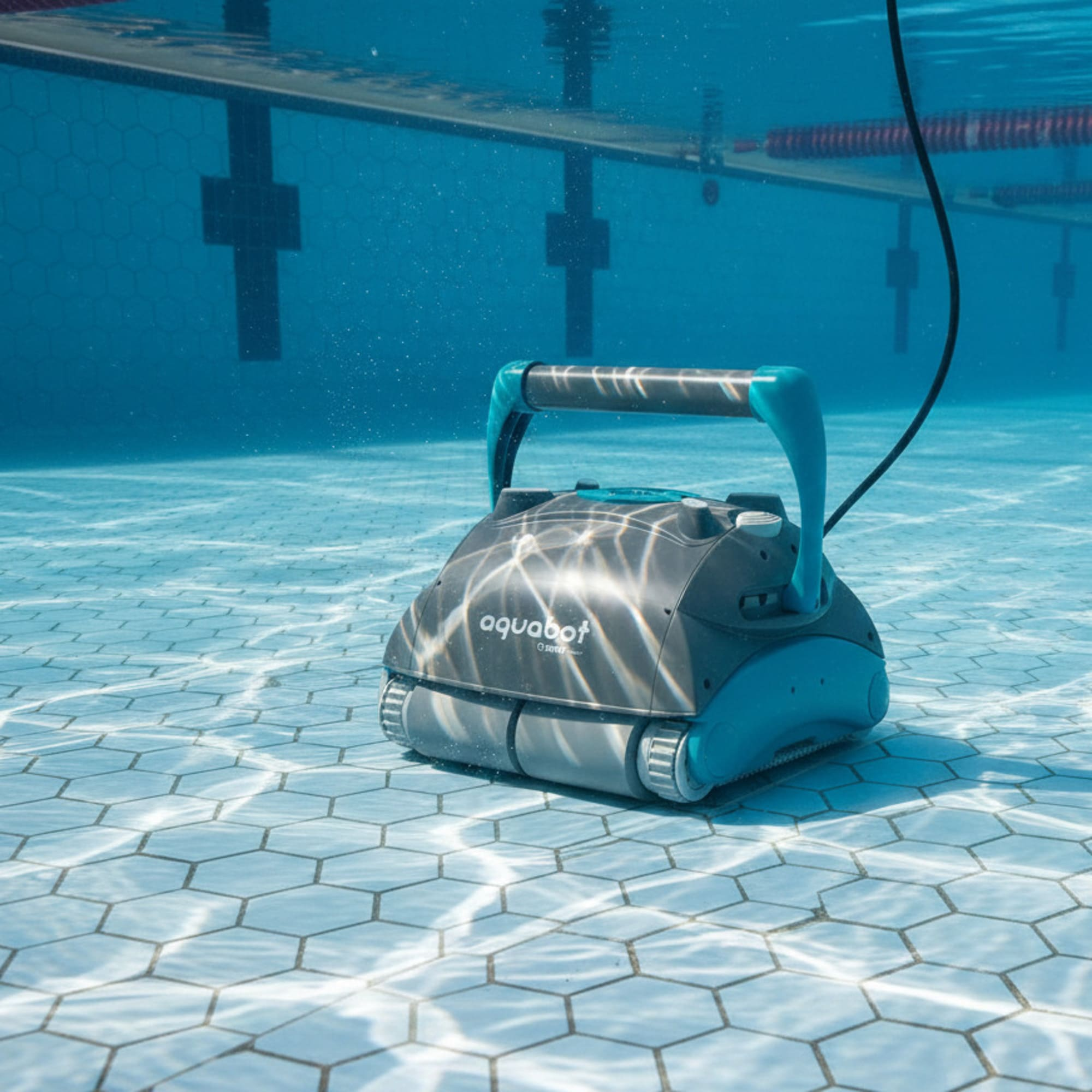 Un robot limpiafondos azul y gris flota sobre el suelo de una piscina embaldosada.