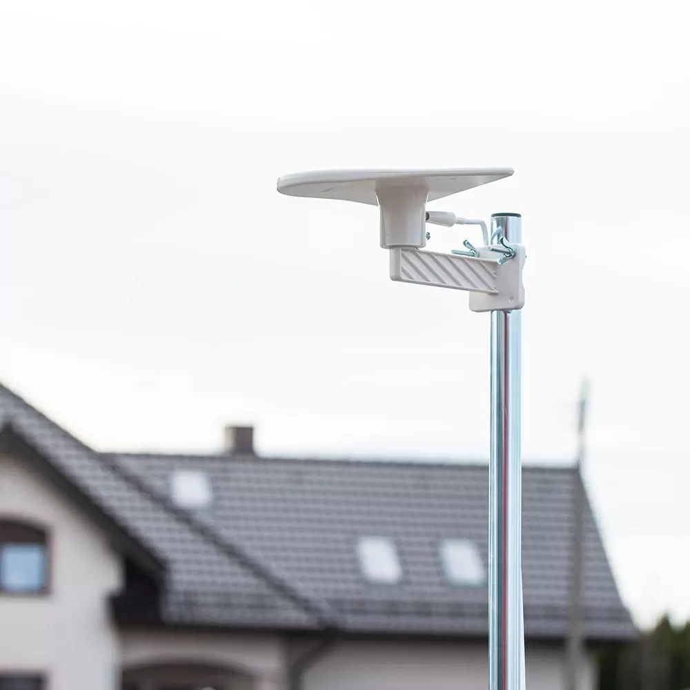 Biała antena satelitarna na metalowym maszcie przed domem z dachówką.