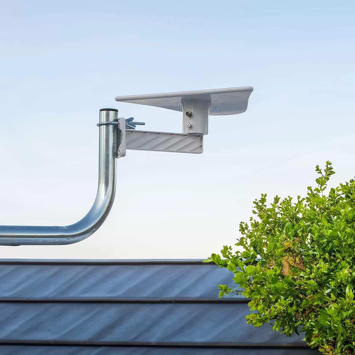 Szary wysięgnik anteny zamontowany na dachu z niebieskim niebem i zielenią.