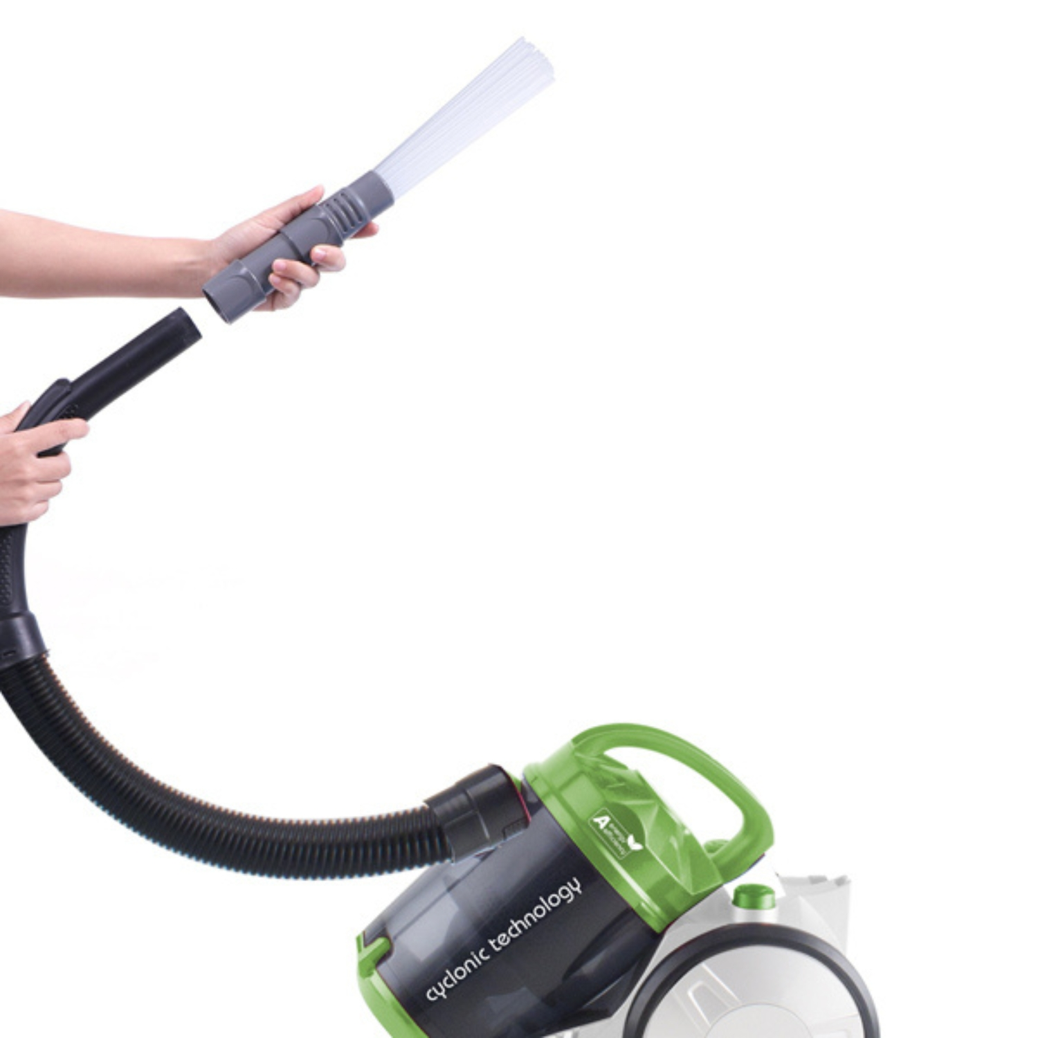 Le mani attaccano un ugello a spazzola a un tubo dell'aspirapolvere collegato a un aspirapolvere verde e bianco.