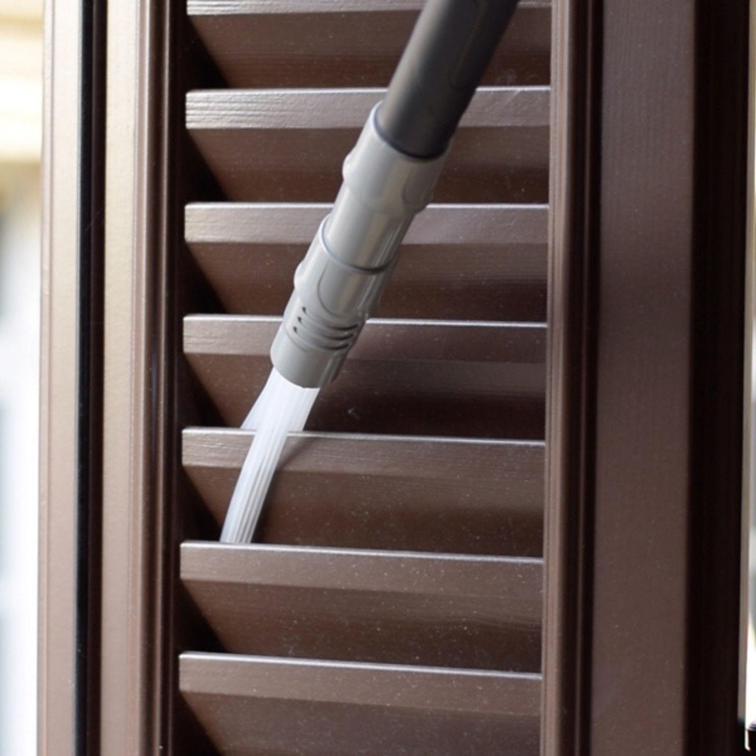 Un accessorio per aspirapolvere pulisce le lamelle di un otturatore marrone.