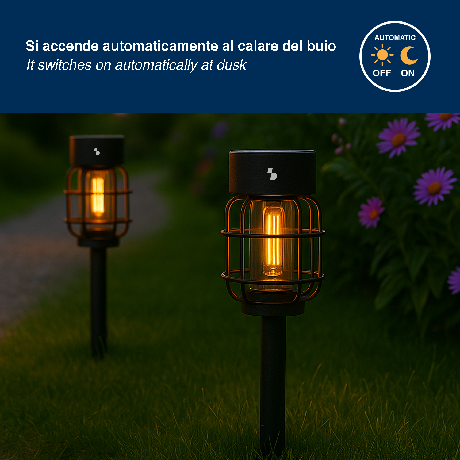 Due lampade da giardino illuminate sull'erba, una a fuoco. Fiori viola sullo sfondo.