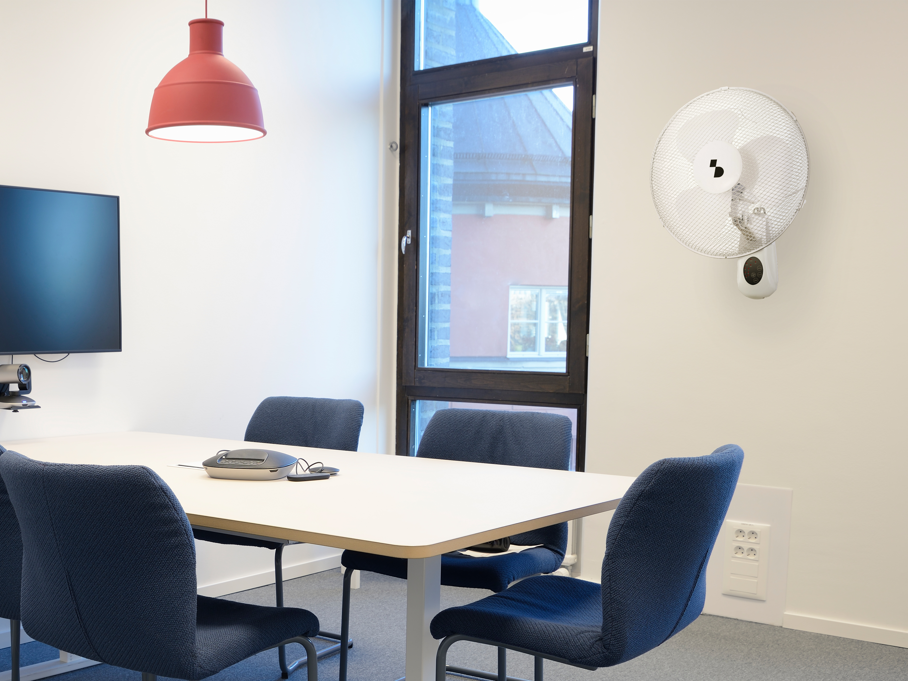 Una sala conferenze con tavolo, sedie, schermo, lampada e ventilatore a parete.