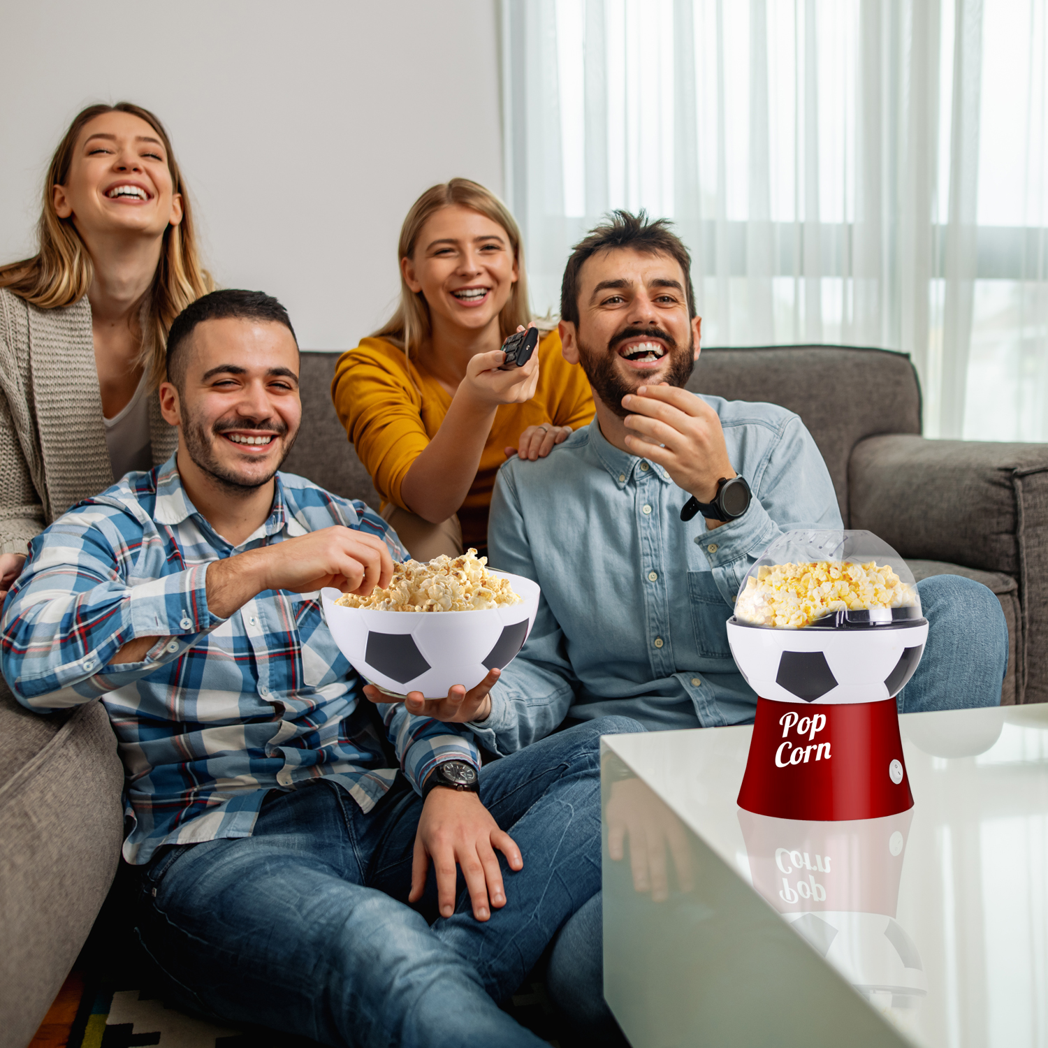 Amici ridono guardando la TV, mangiando popcorn da una ciotola da calcio e una macchina per popcorn.