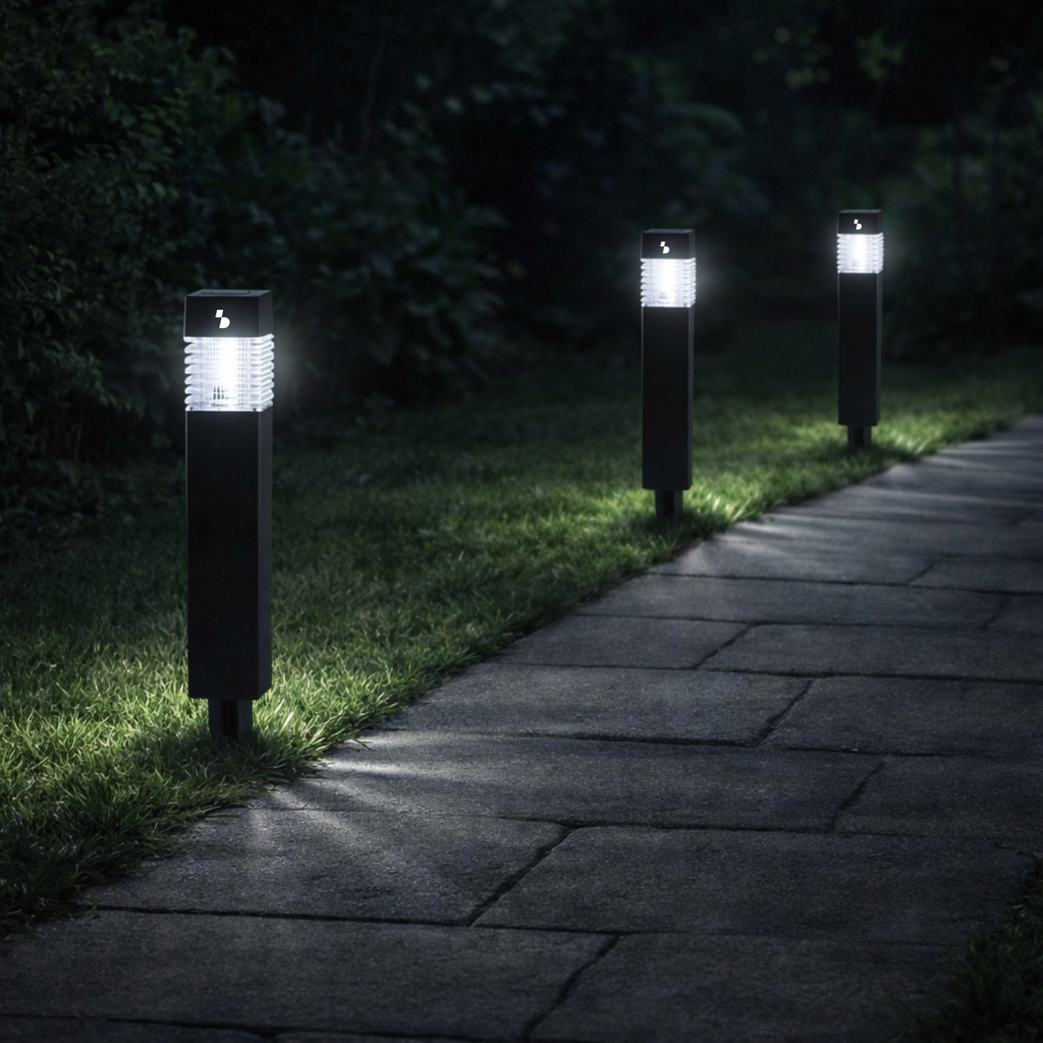 Tre moderne luci da sentiero illuminano un vialetto al buio.