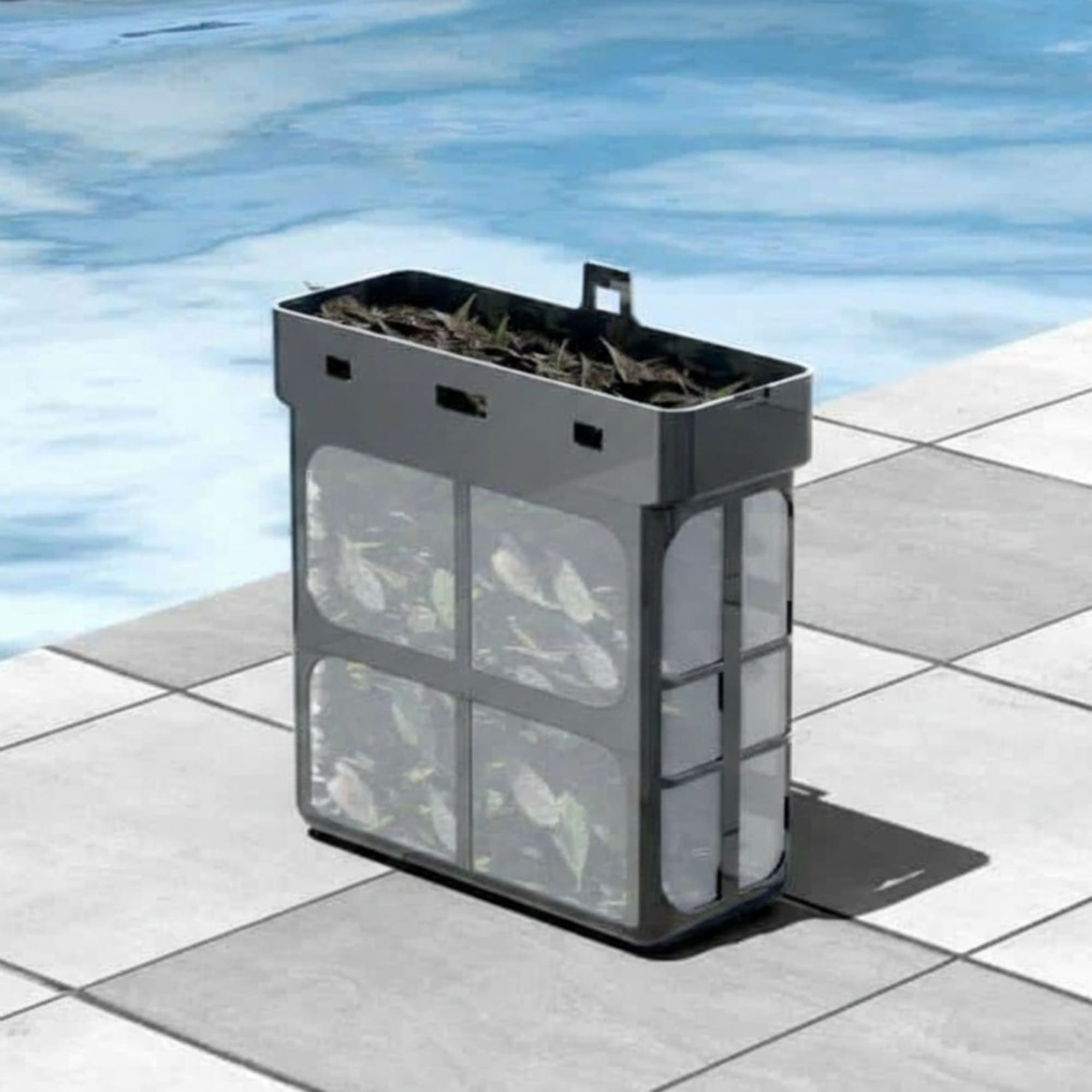 Un cestello raccogli foglie grigio per piscina pieno di foglie è vicino a una piscina blu.