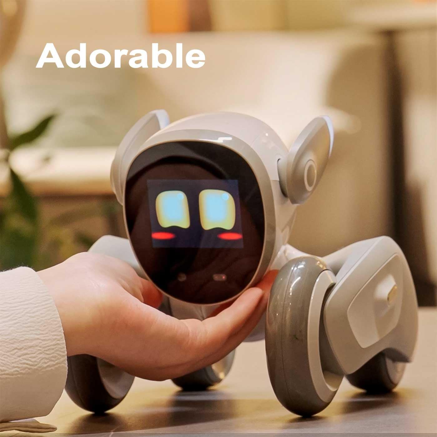 Una mano sostiene un pequeño robot blanco con ruedas y una pantalla que muestra ojos.