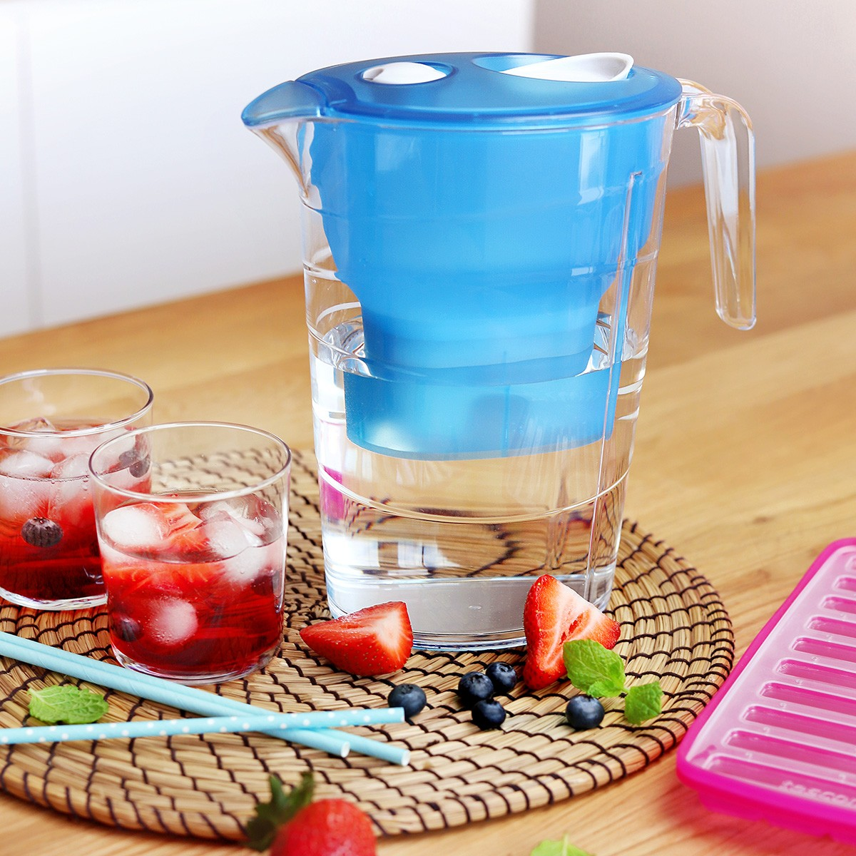 Ein blauer Wasserfilterkrug mit Früchten und Eiswasser in Gläsern.