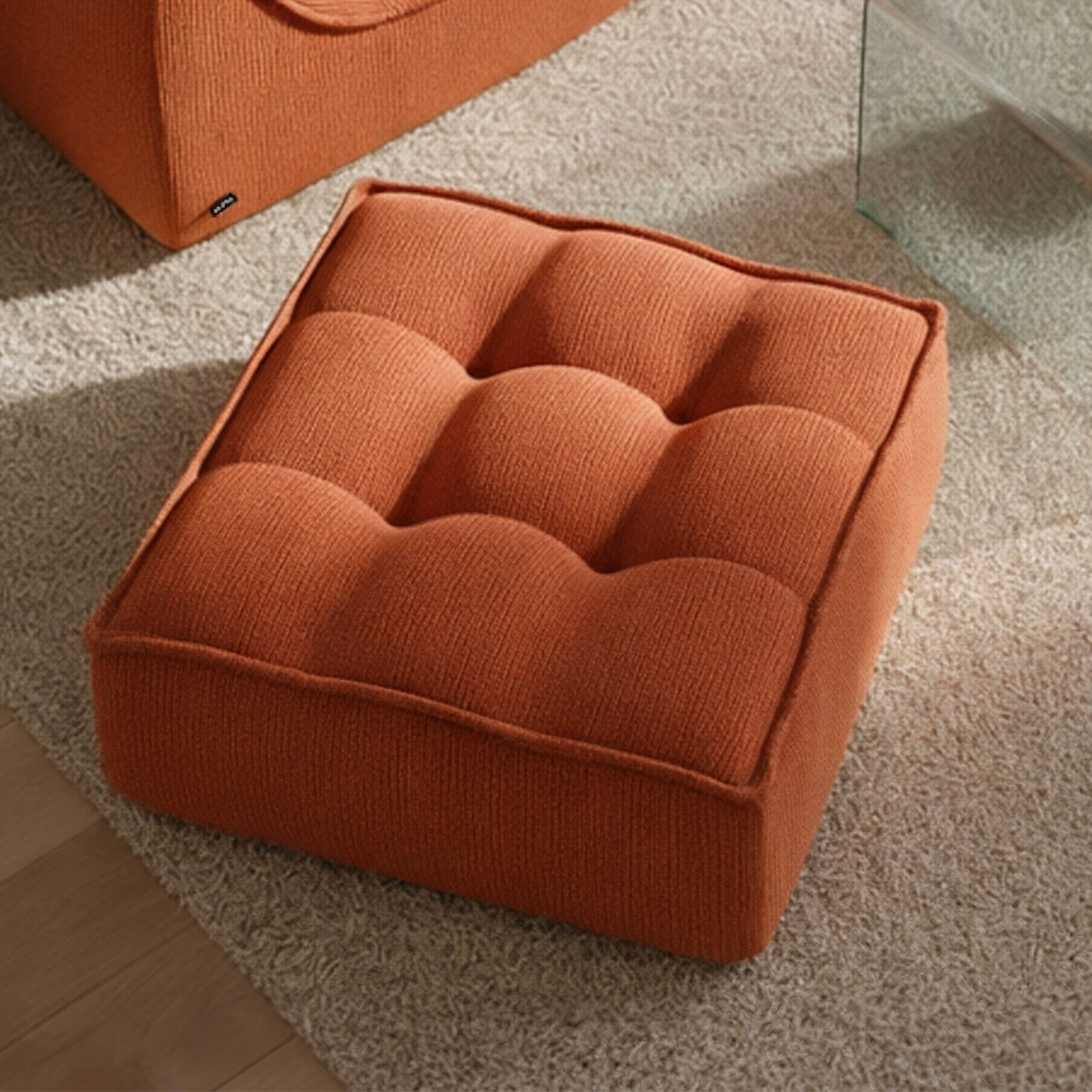 Ein orangefarbener Hocker mit Knopfpolsterung auf einem Teppich.
