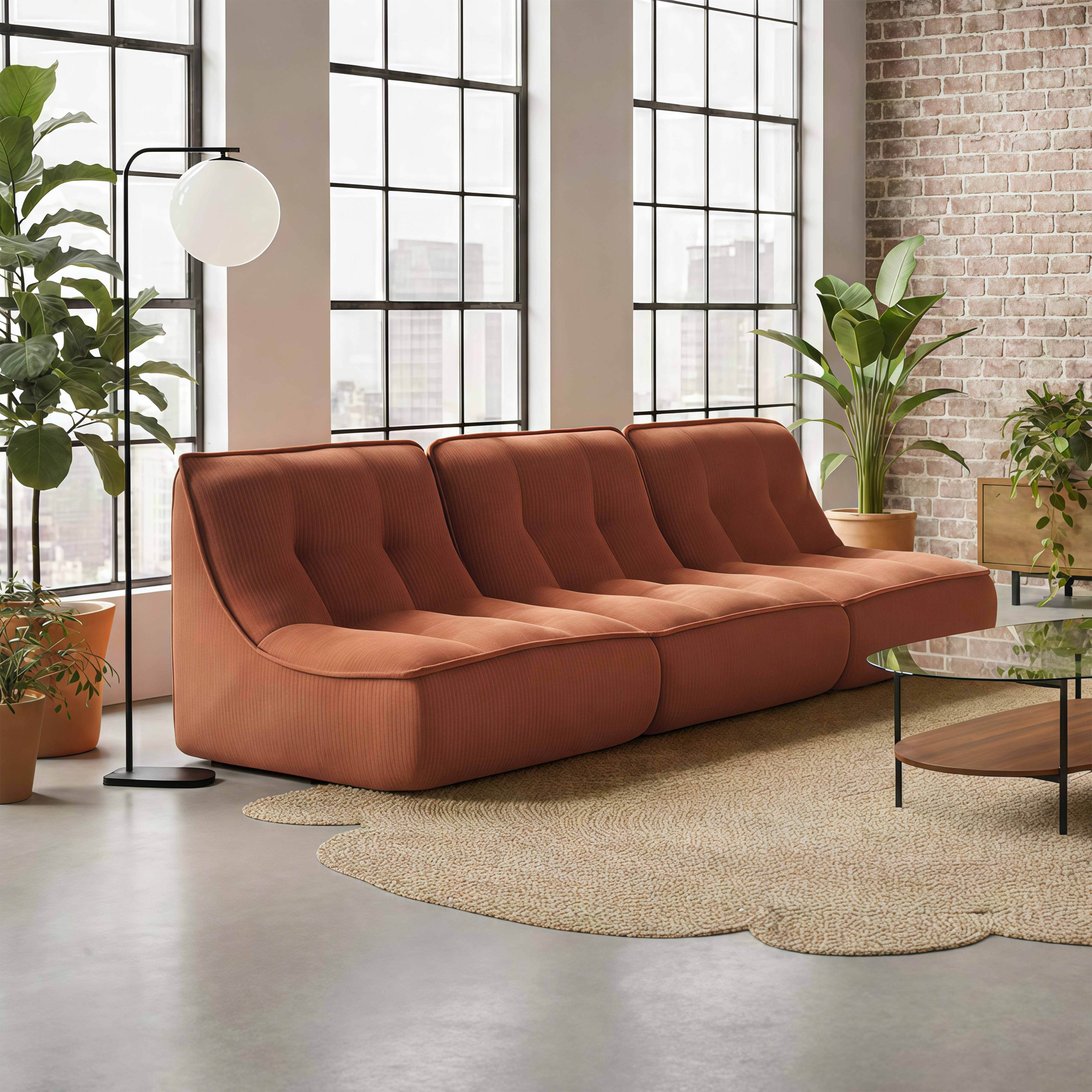 Ein orangefarbenes Sofa mit Rillen steht vor großen Fenstern in einem Raum mit Ziegelwand.