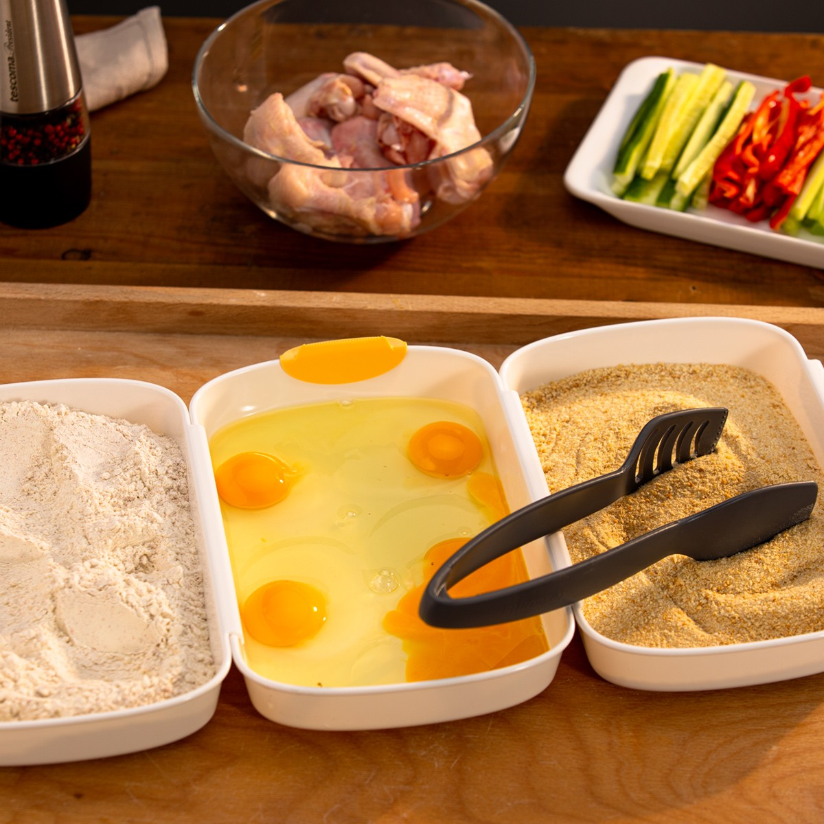 Pezzi di pollo crudi, farina, uova e pangrattato per la preparazione.