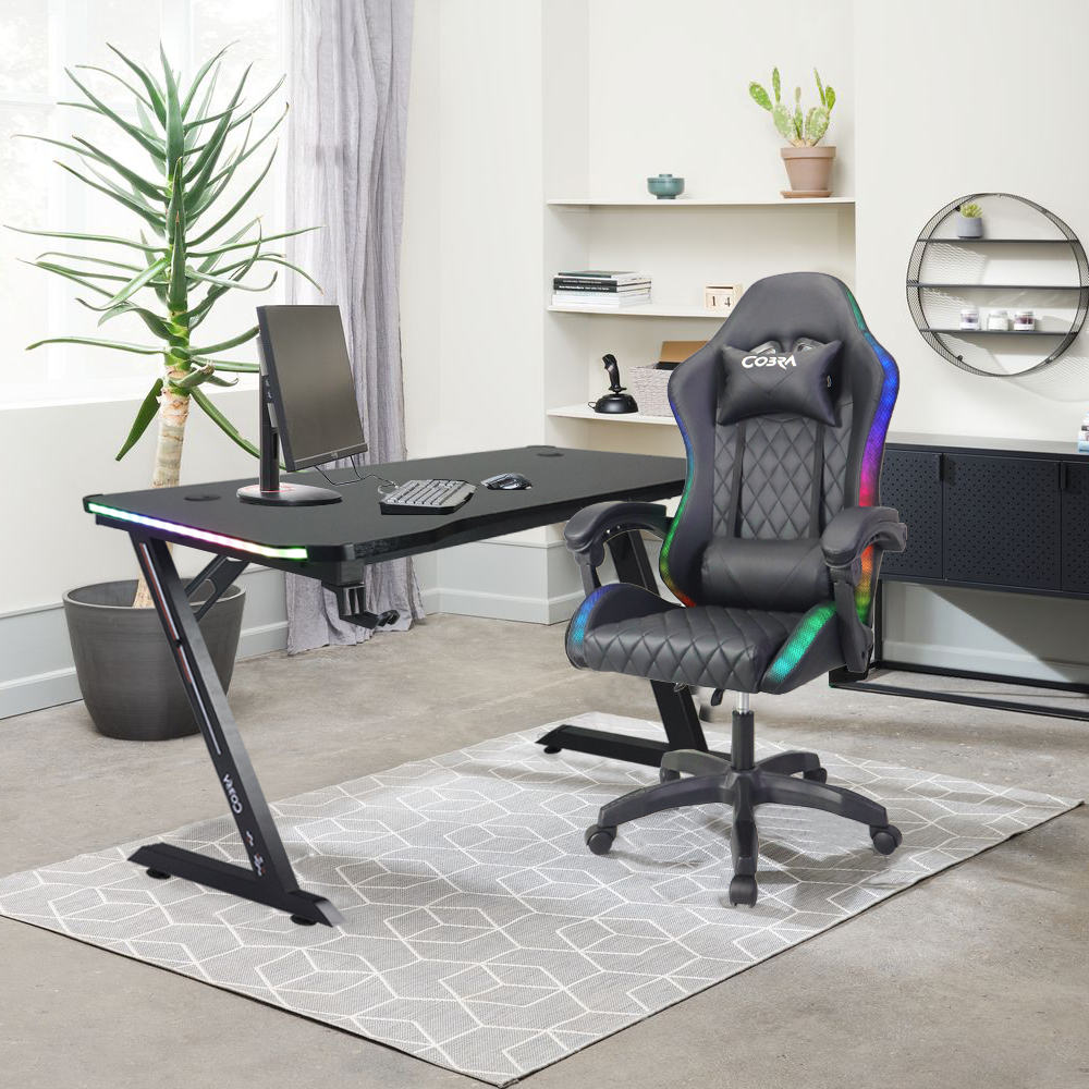 Czarne biurko gamingowe z oświetleniem RGB, monitorem i fotelem gamingowym.