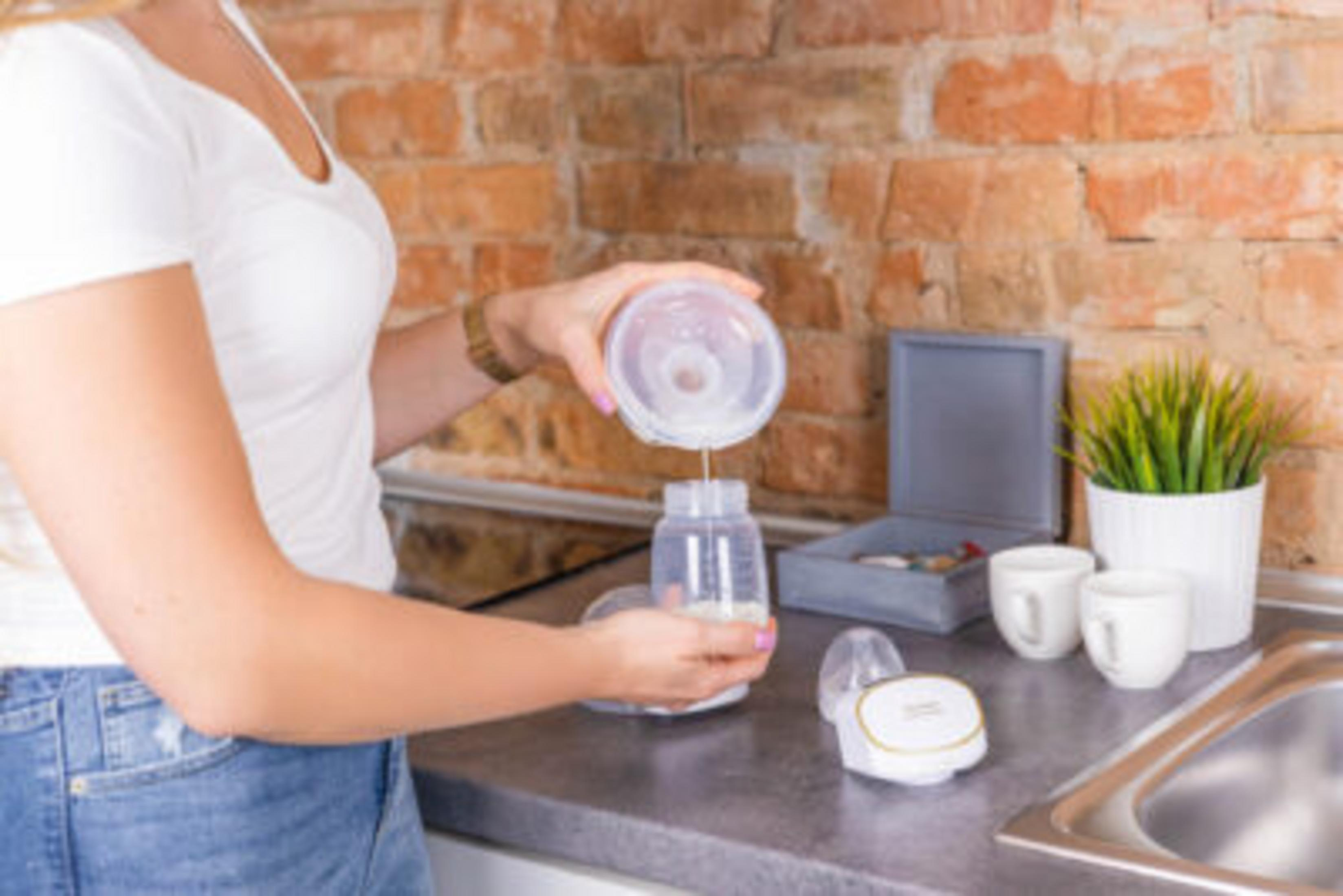 Una donna versa latte in polvere in un biberon, con tazze nelle vicinanze.