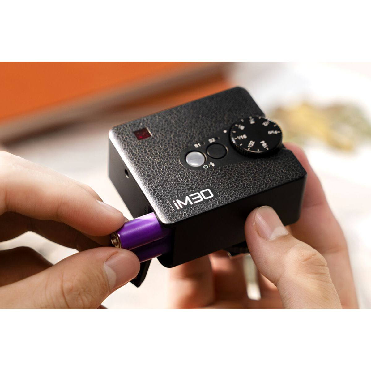 Eine Hand setzt eine violette Batterie in ein schwarzes iM30-Gerät ein.