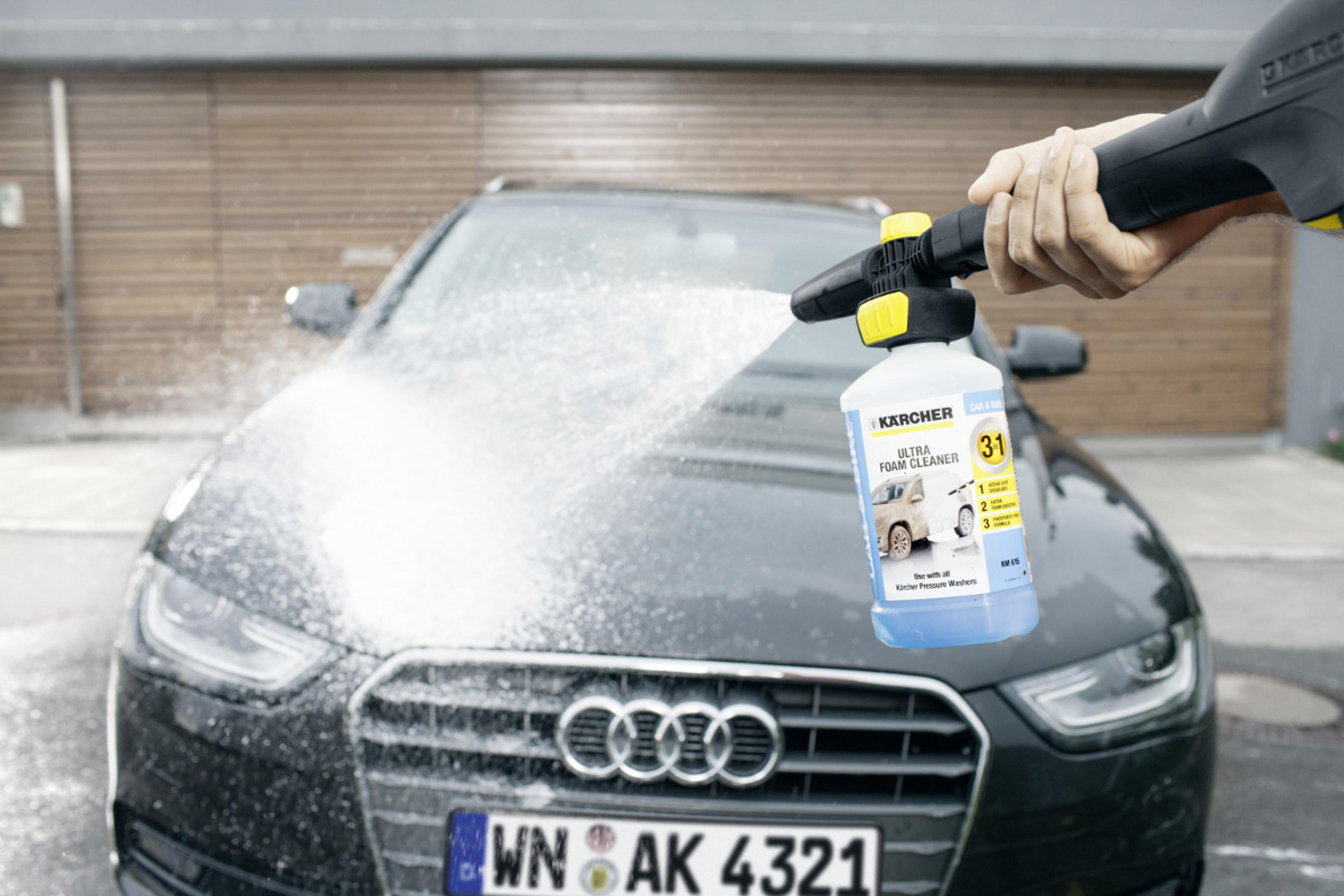 Un pulitore schiumogeno Kärcher spruzza un'auto scura lavata all'aperto.